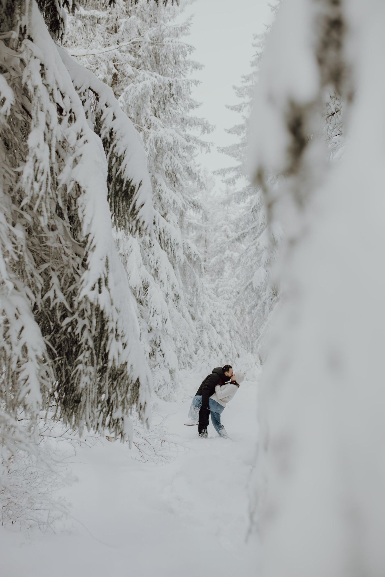 Person hiking through a snow-covered winter forest with frost-laden evergreen trees lining the path.