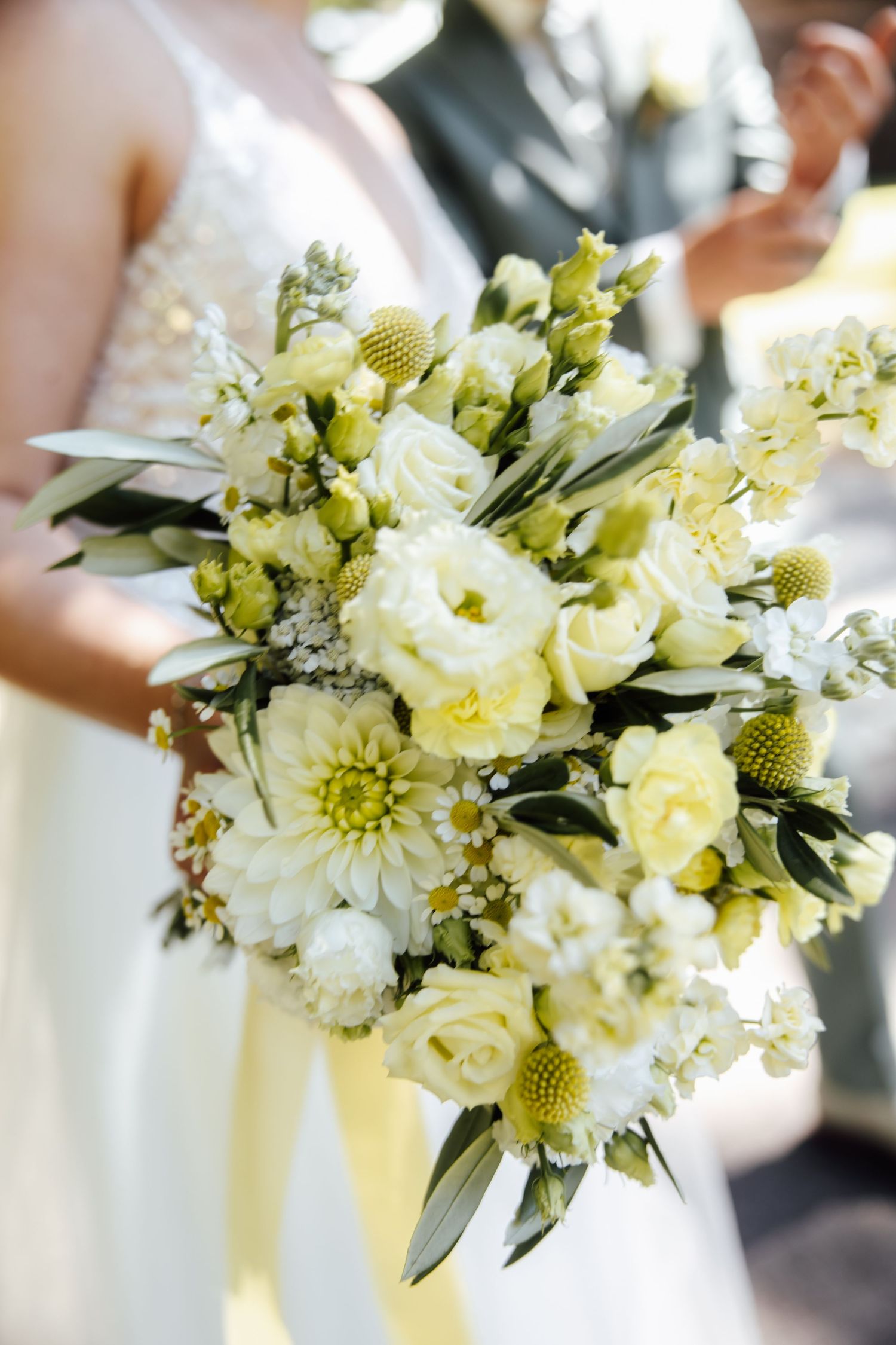 Bride holding a lush white and yellow wedding bouquet with roses, dahlias, and greenery on her special day.