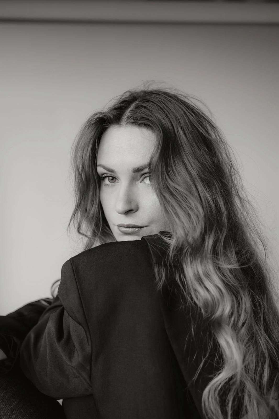 Elegant black and white portrait of a young woman with long wavy hair in a dark outfit.
