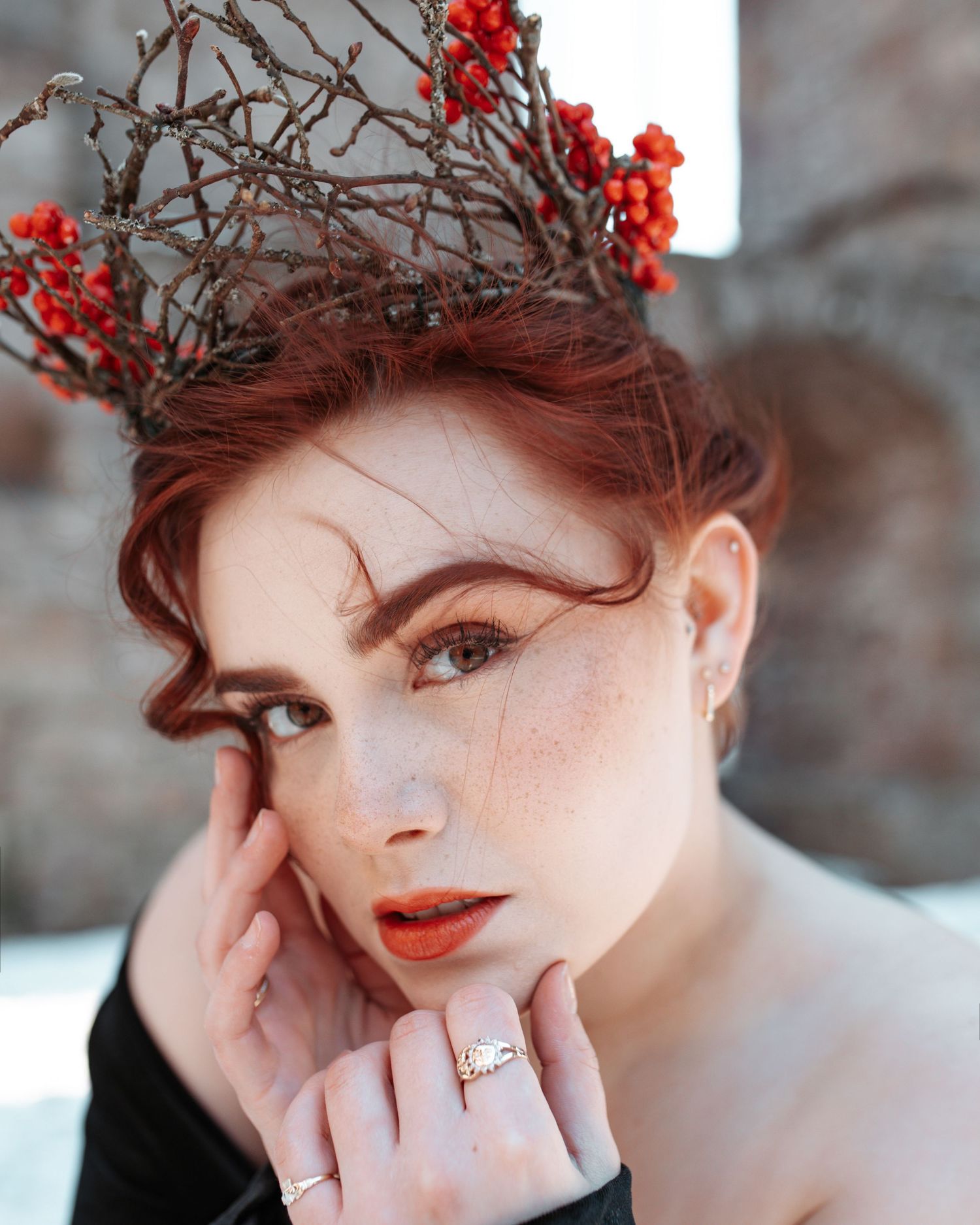 Redhead woman with freckles wearing a twig and berry crown with bold orange lipstick outdoors.