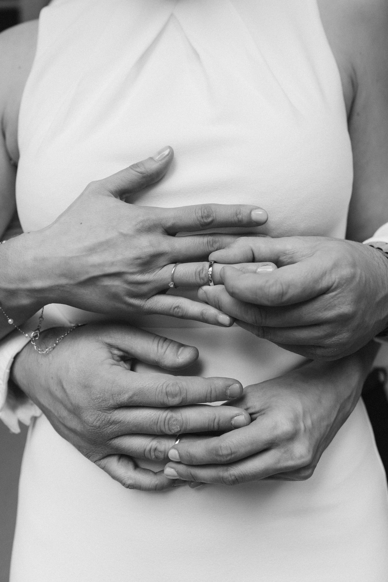 Black and white close-up of bride and groom hands with wedding rings embracing at waist.