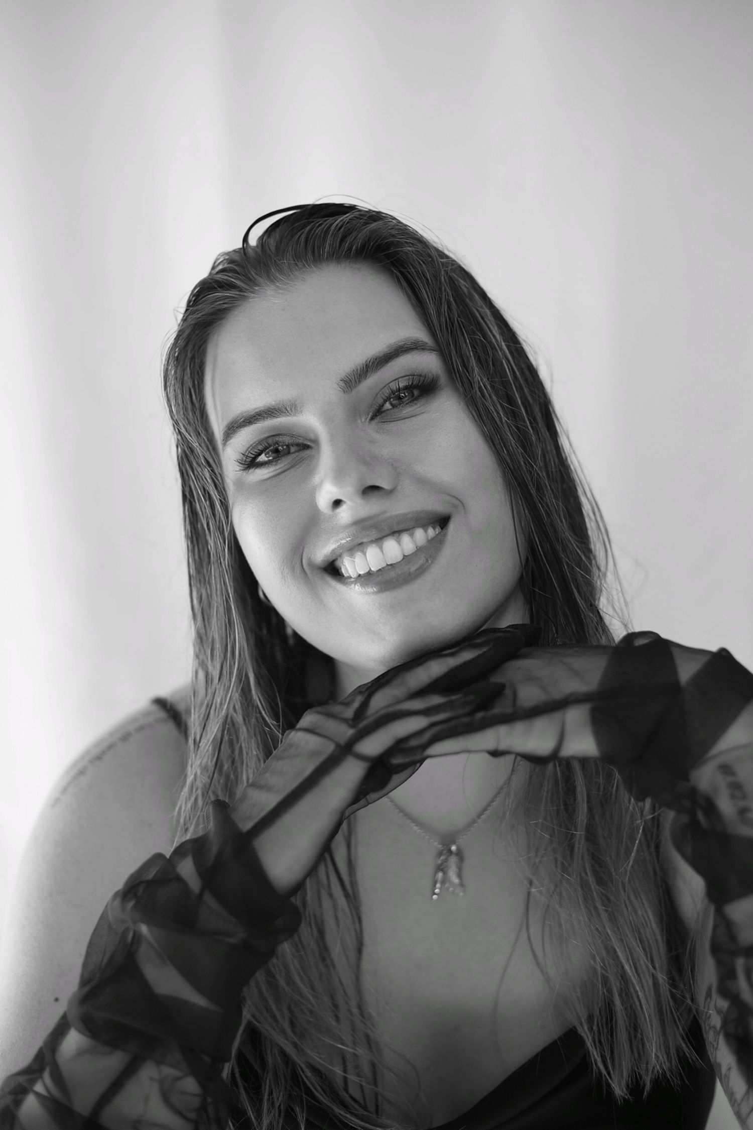 Black and white portrait of a smiling young woman with long hair wearing a sheer black top.