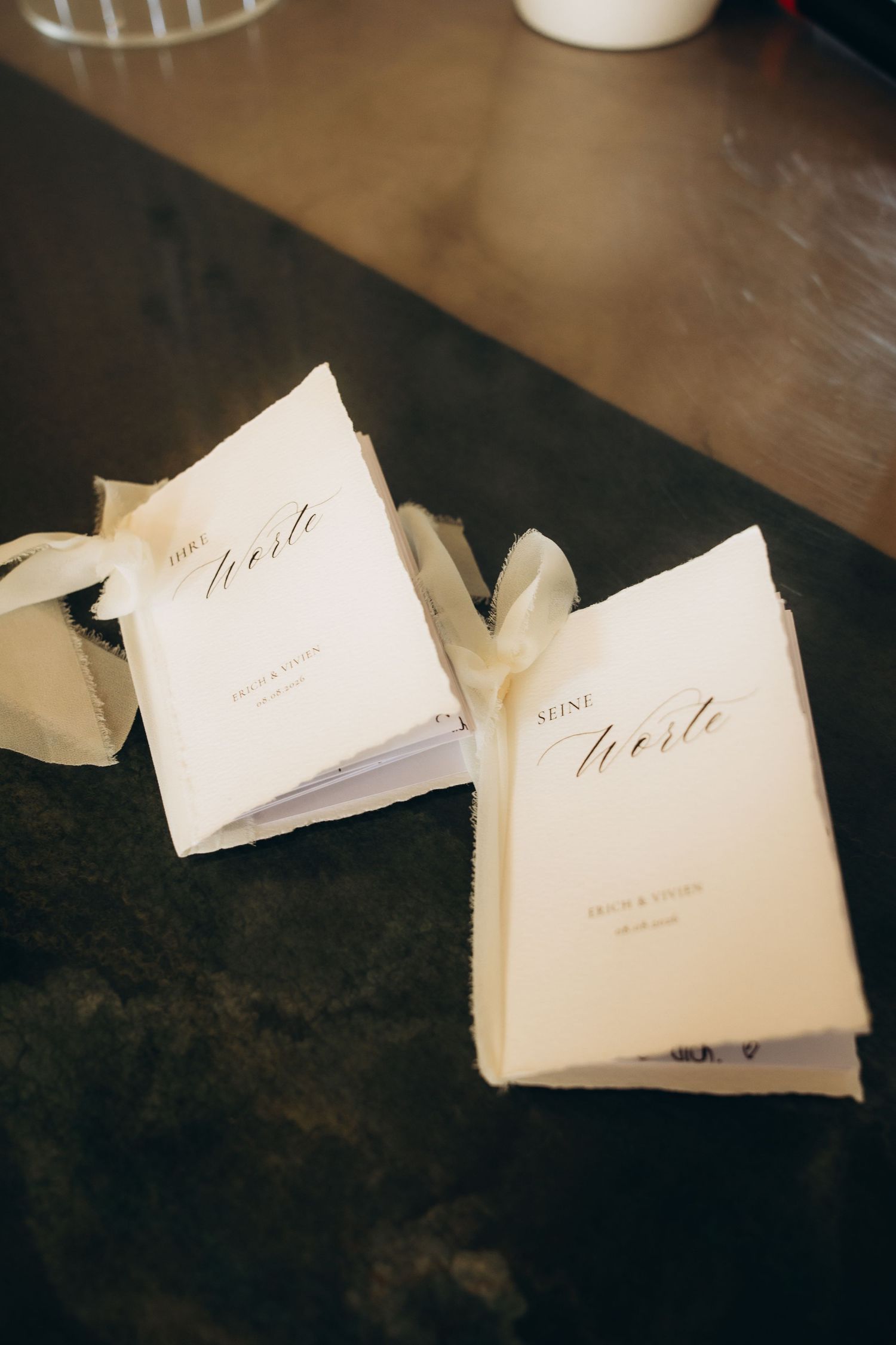 Two elegant white wedding vow booklets tied with ribbon, labeled 