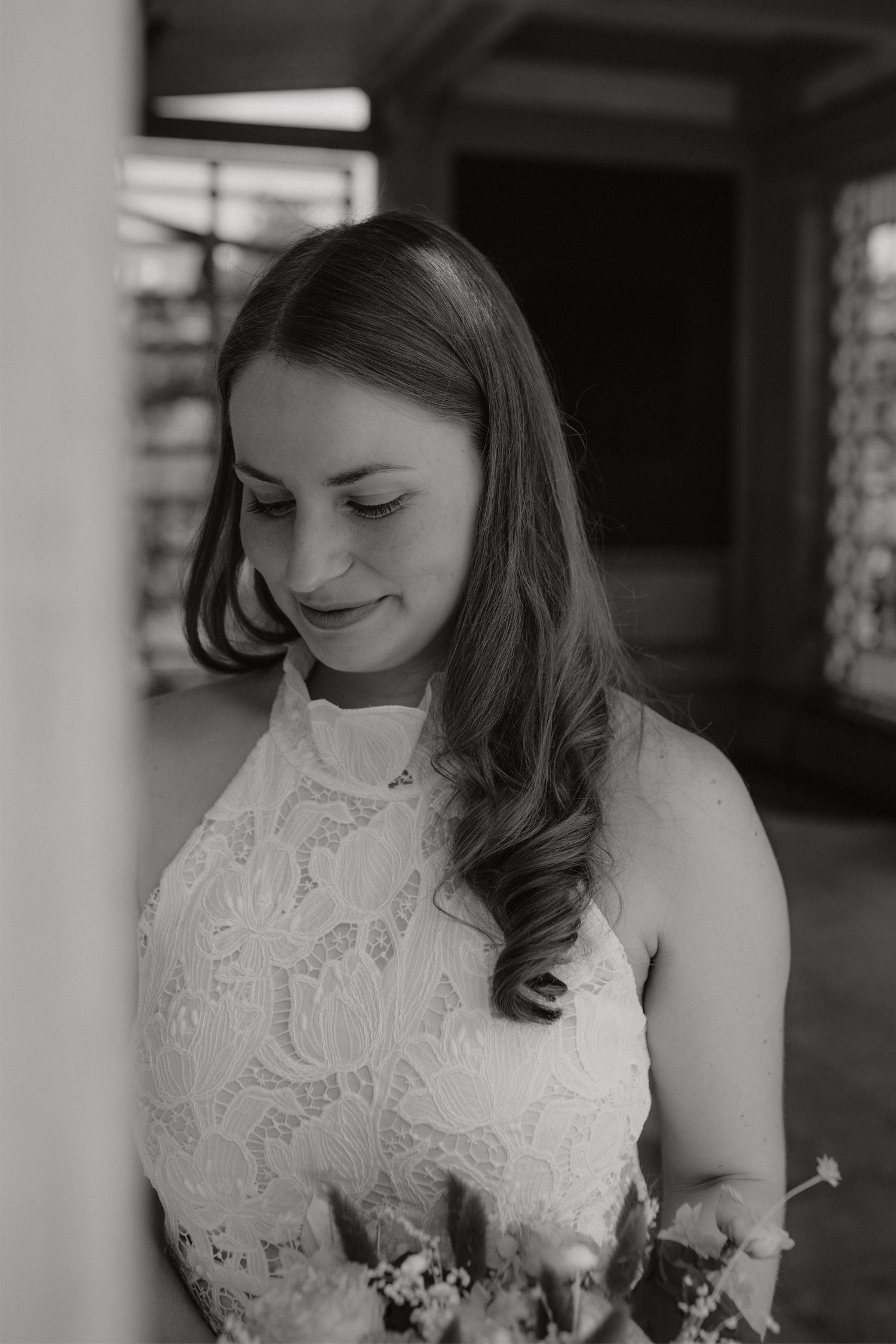 Black and white portrait of a smiling bride in a lace halter wedding dress looking downward.