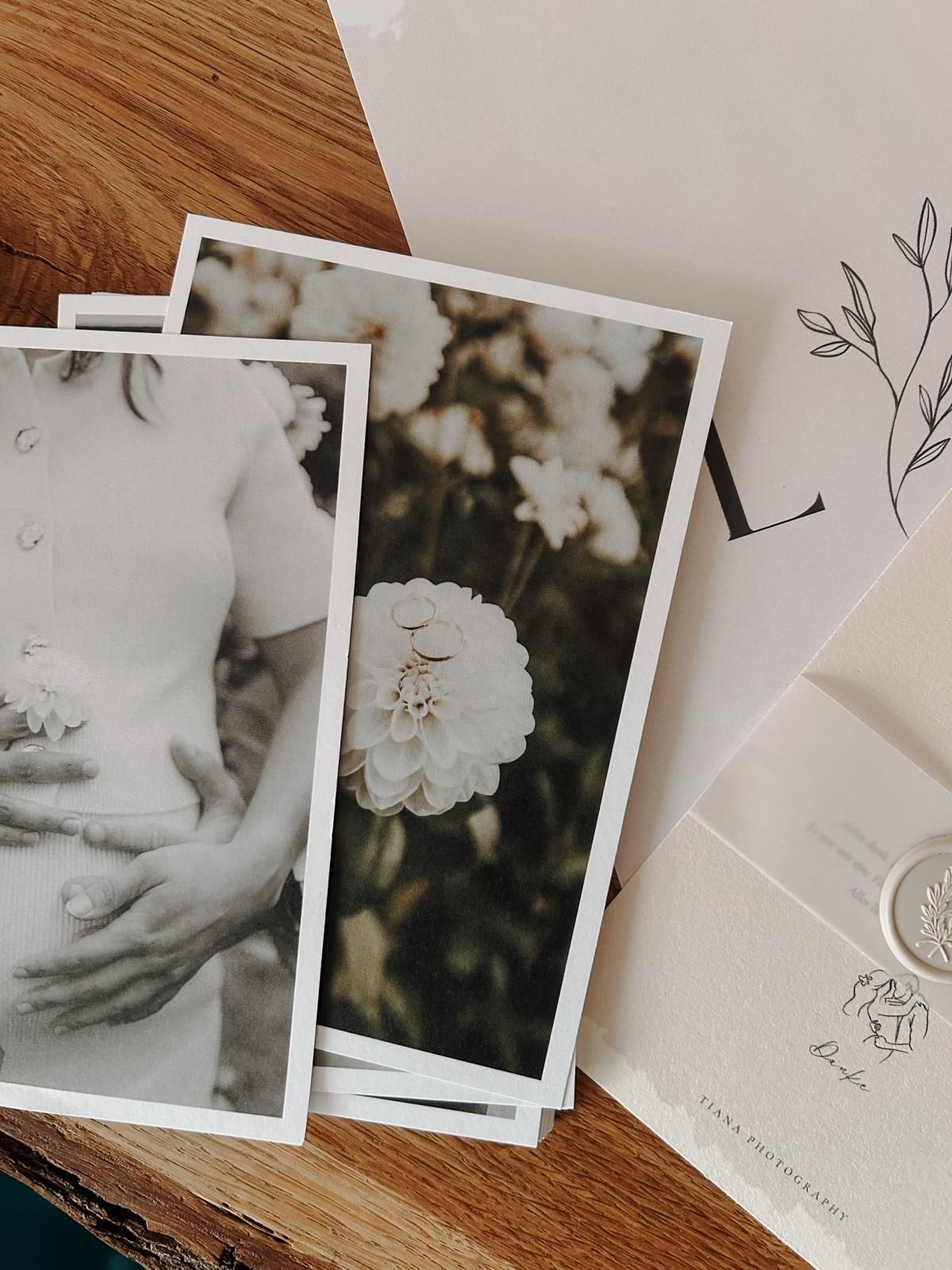 Elegant wedding photography prints and stationery with floral details arranged on a wooden surface.