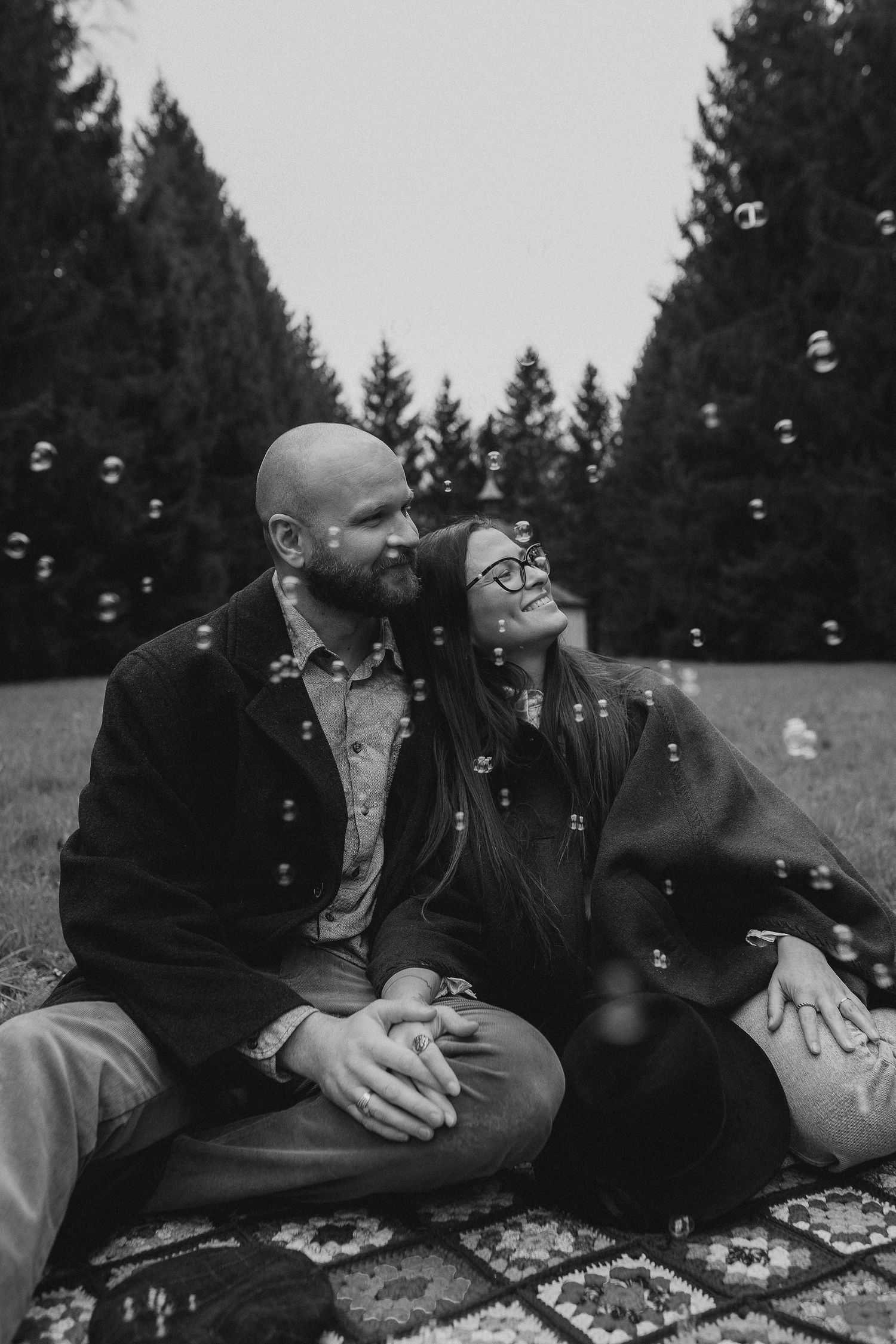 Black and white photo of couple sitting on blanket surrounded by bubbles.