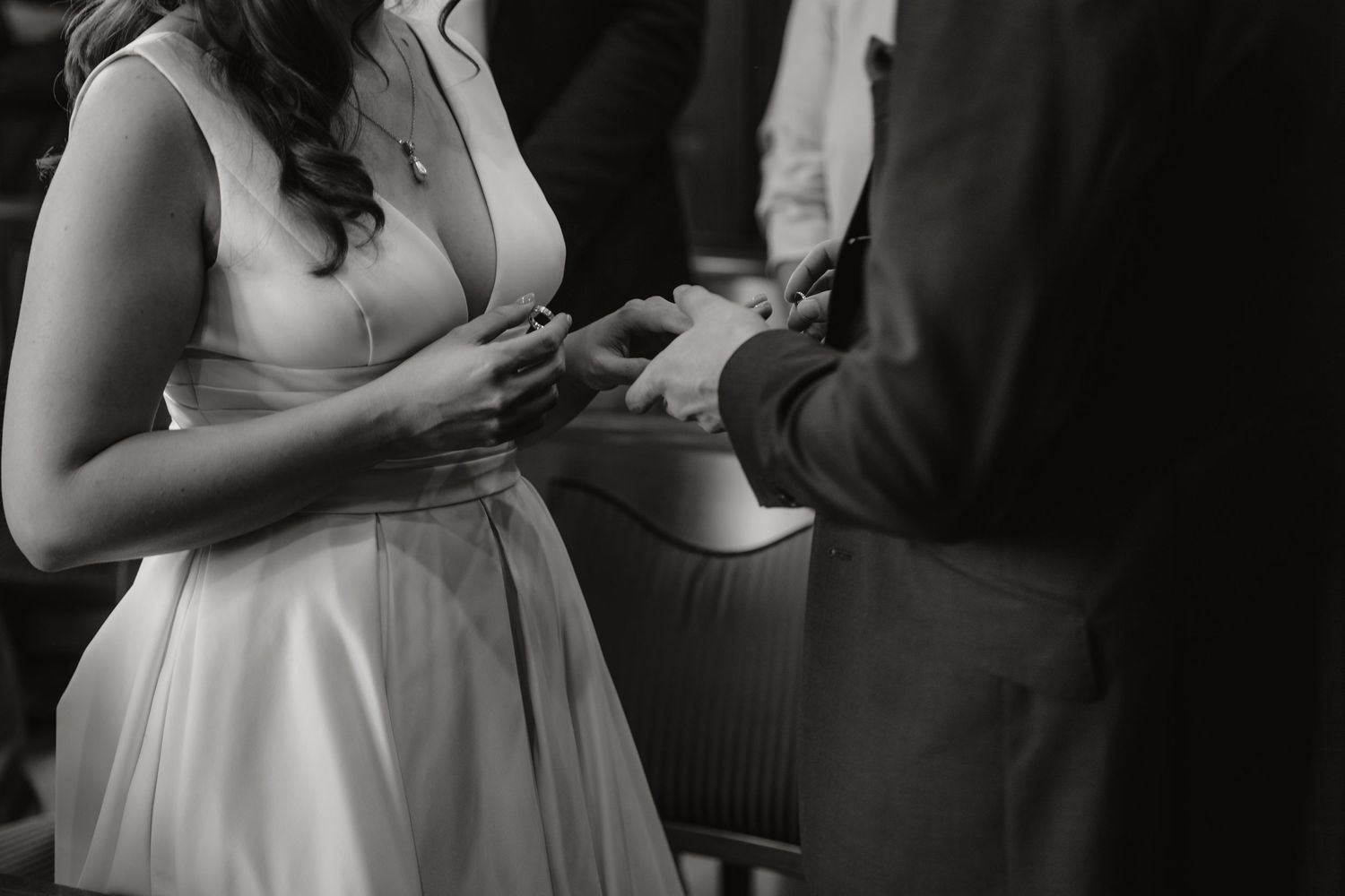 Black and white photo of bride placing wedding ring on groom's finger during ceremony.
