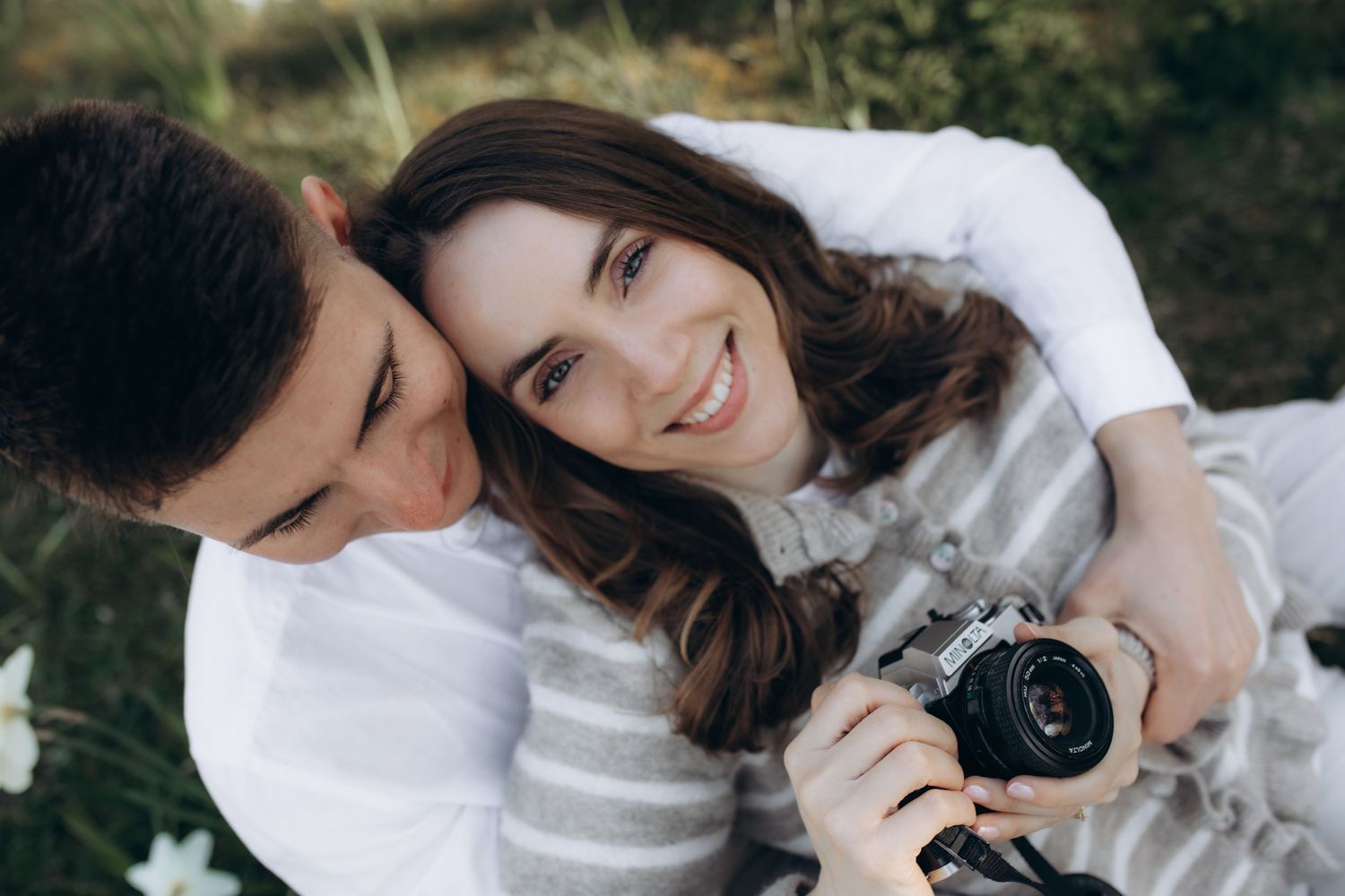 Happy couple smiling together outdoors, woman holding a vintage film camera, enjoying a romantic photography session in nature.
