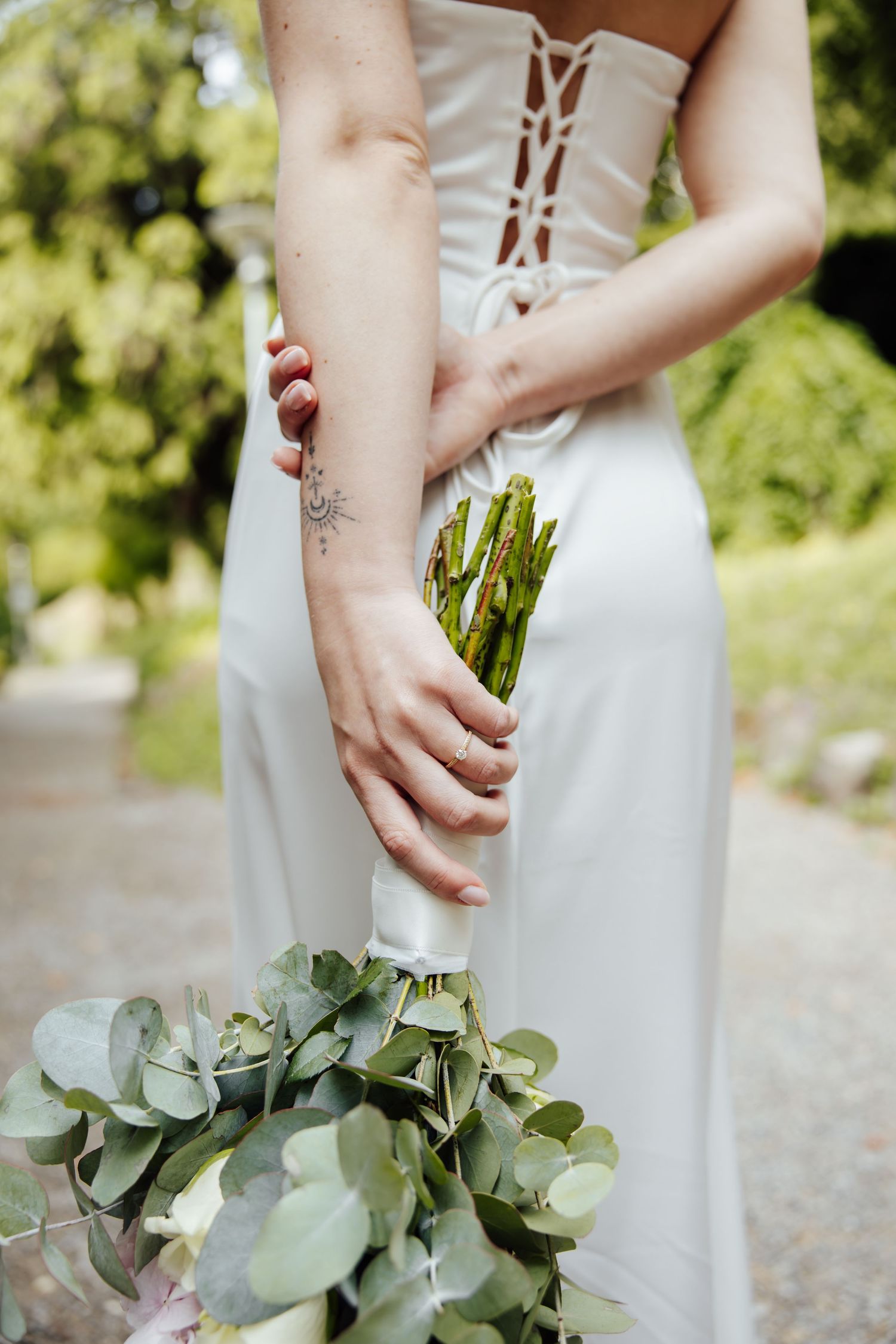 Bride in white strapless gown holding a green eucalyptus bouquet with asparagus, tattoo visible on her arm.