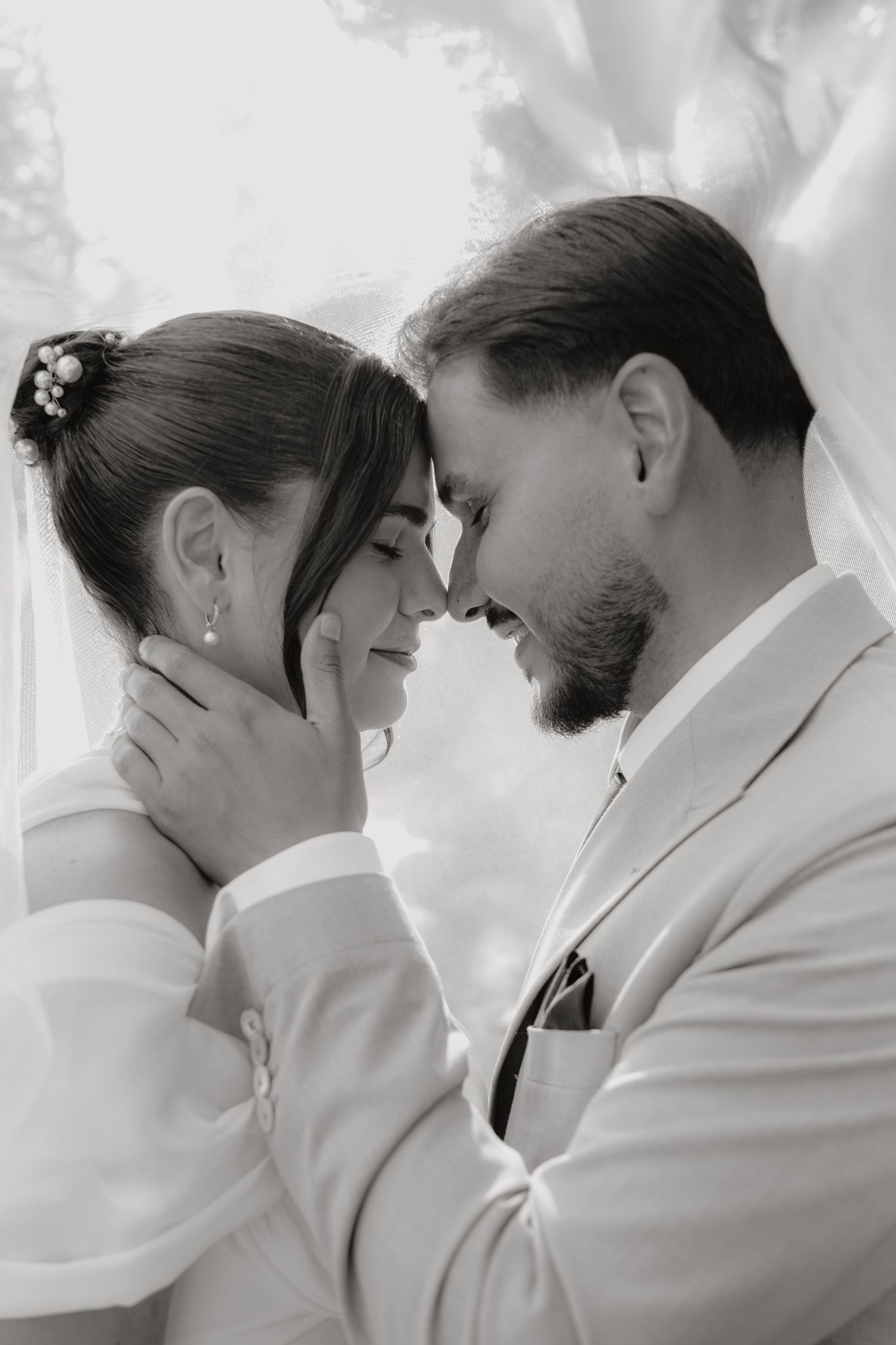 Black and white photo of bride and groom touching foreheads tenderly on wedding day.