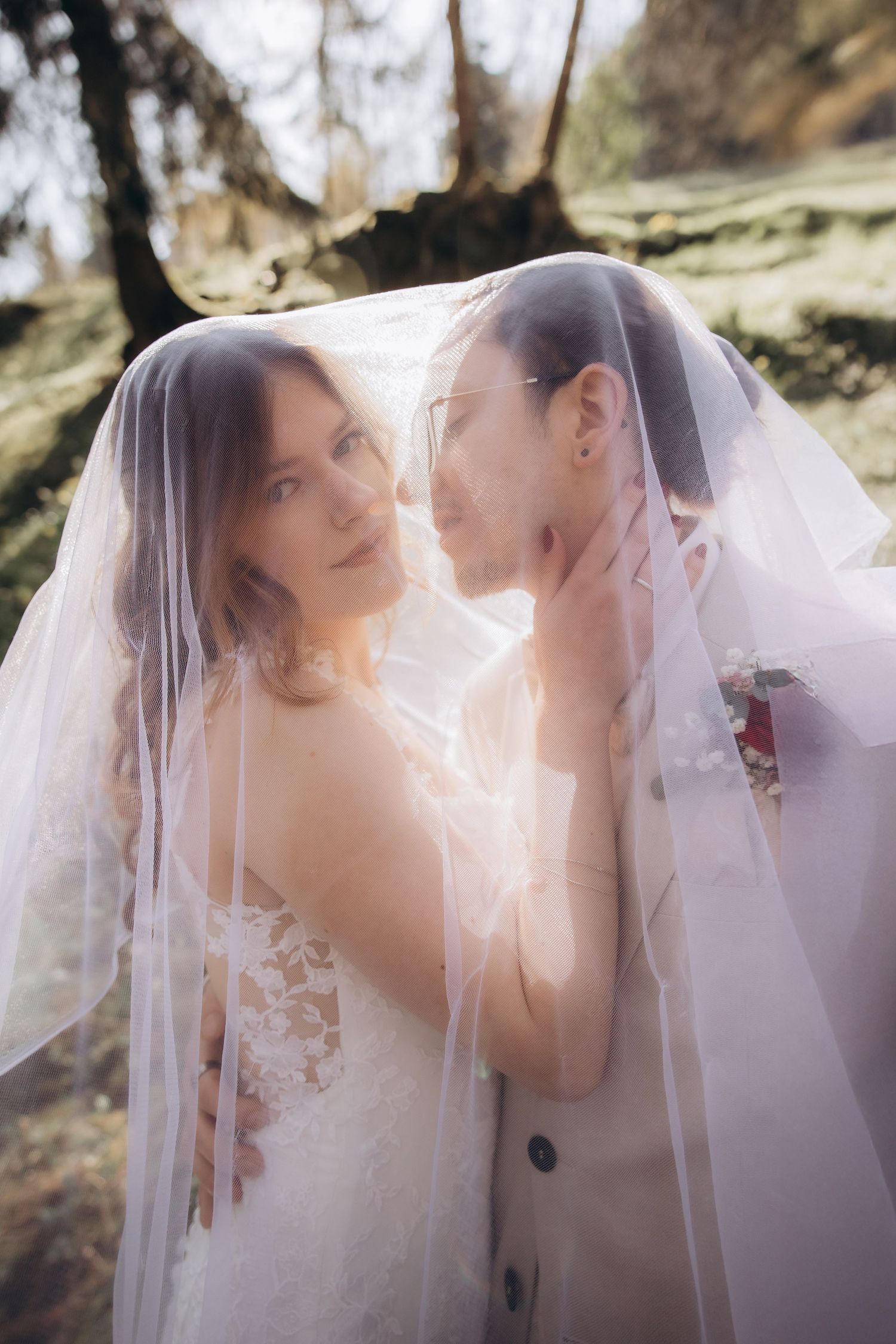 Bride and groom sharing intimate moment together under flowing white wedding veil.