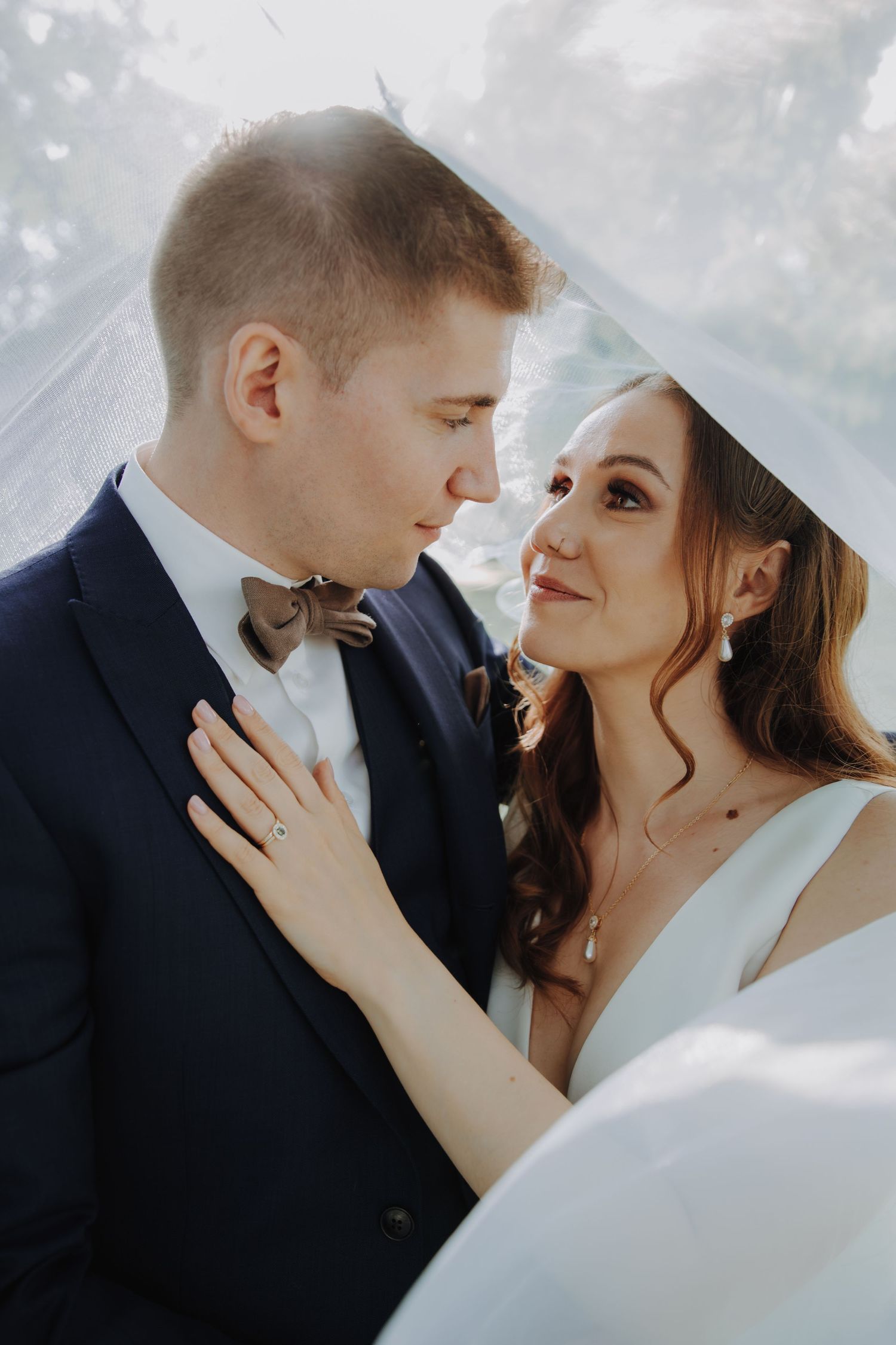 Bride and groom share an intimate moment under a flowing veil with soft natural light.