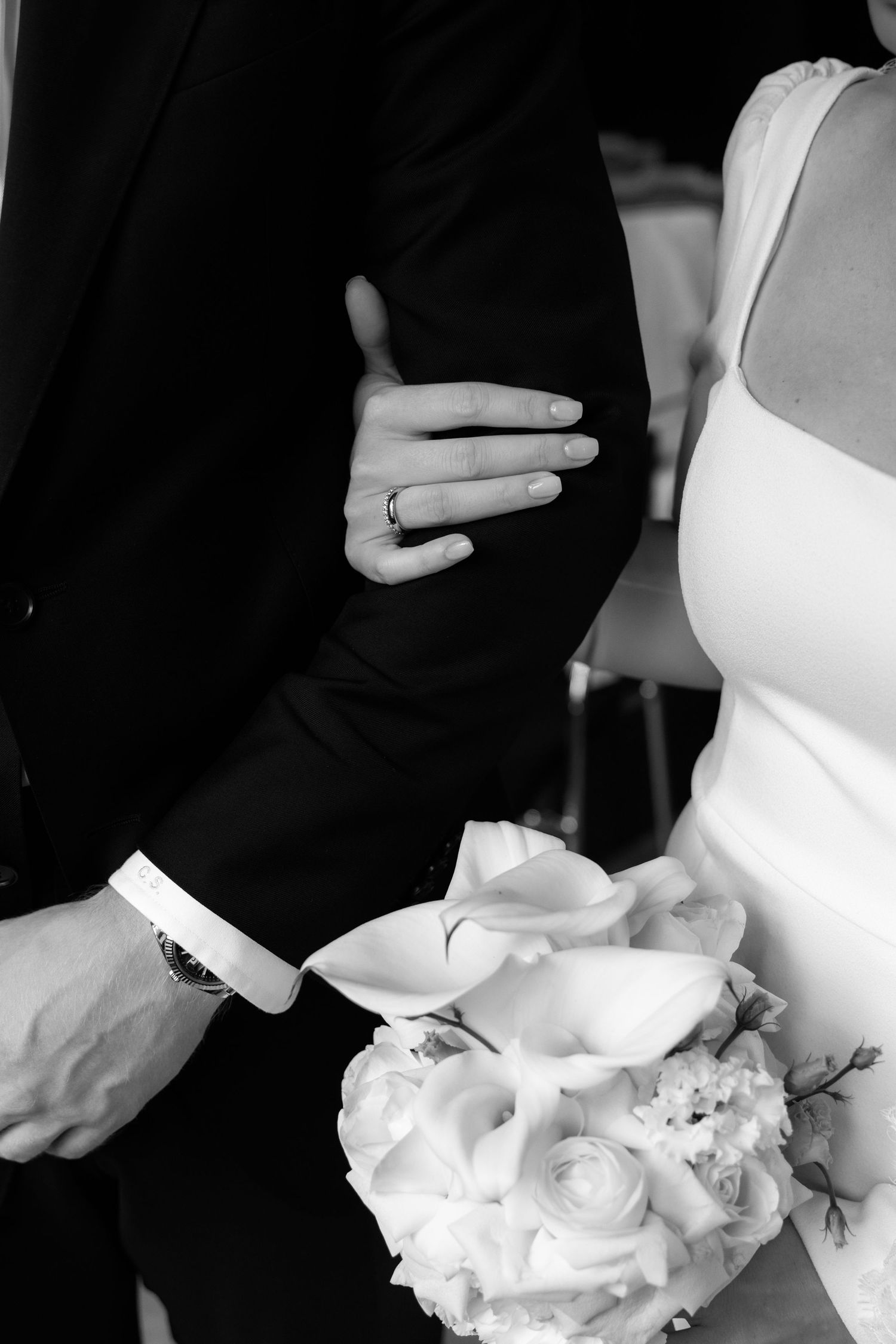 Black and white wedding photo of bride and groom holding bouquet of roses, with wedding ring visible on bride's hand.