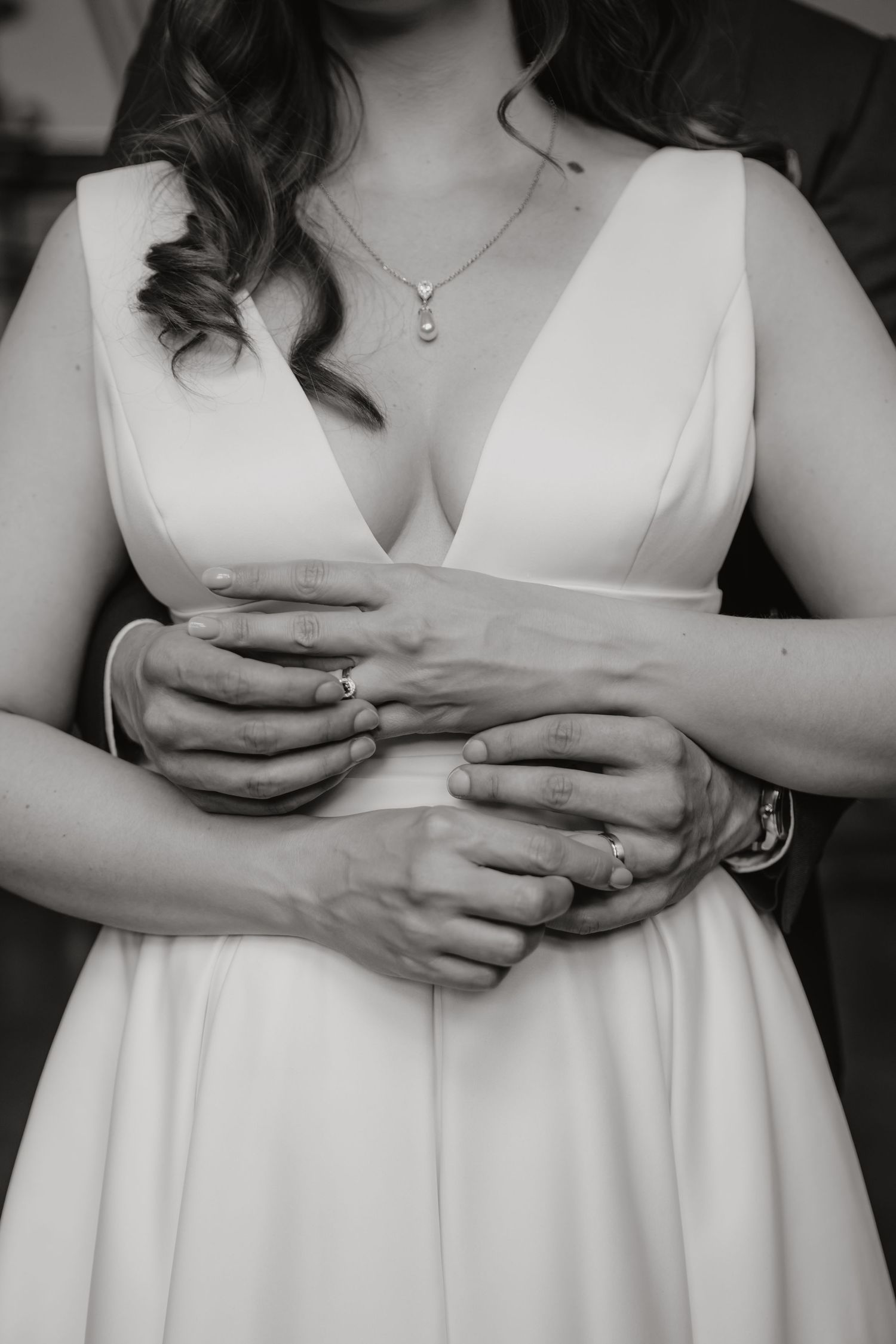 Black and white close-up of bride and groom's hands with wedding rings embracing at the waist.