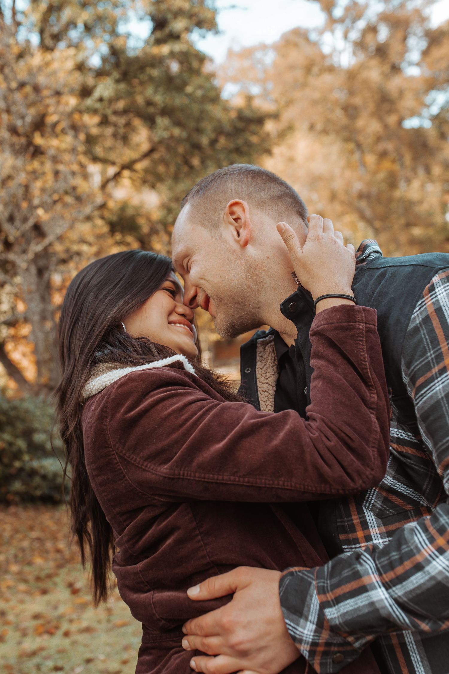Happy couple embracing and smiling nose-to-nose in an autumn park setting.