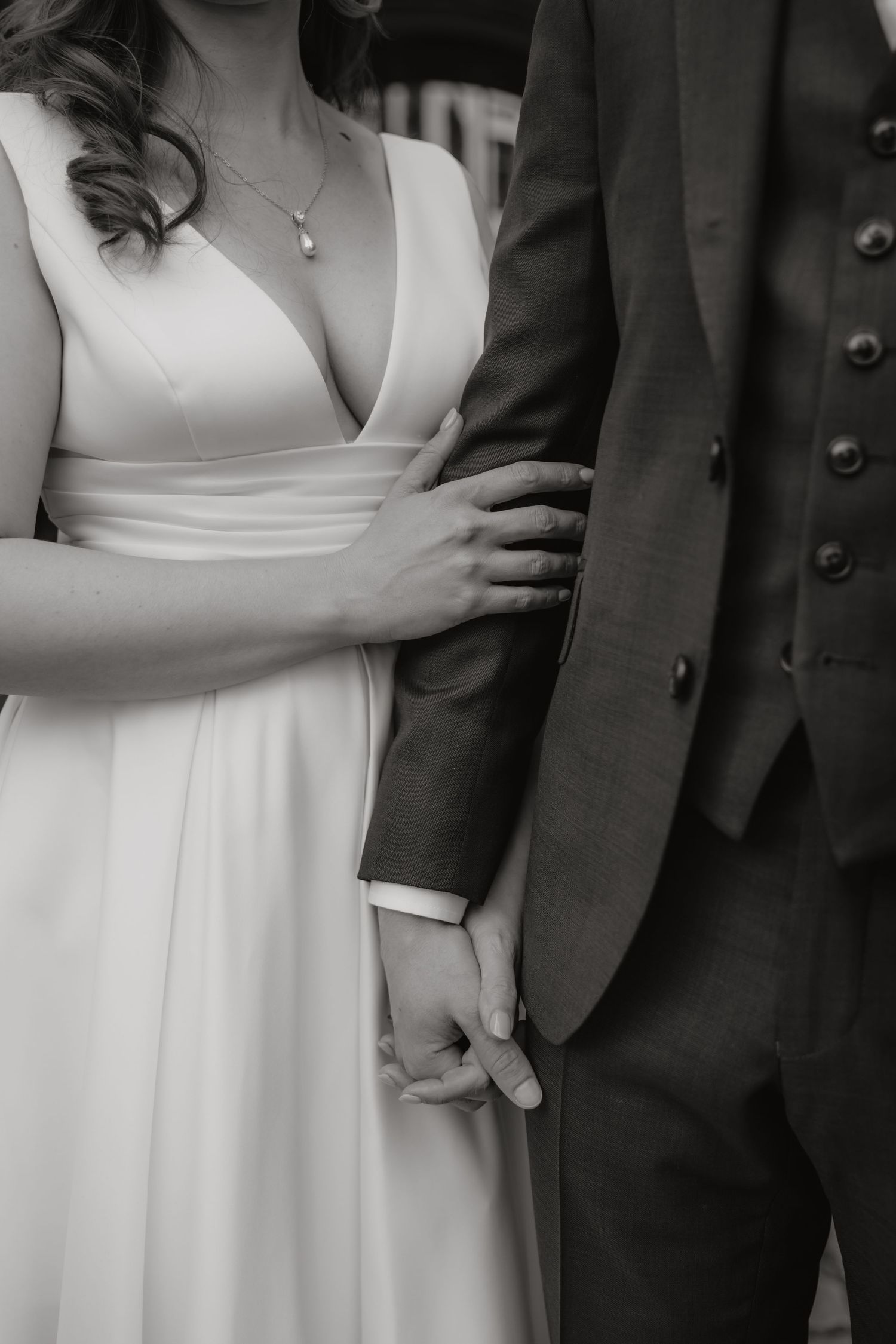 Black and white photo of bride and groom holding hands in elegant wedding attire.