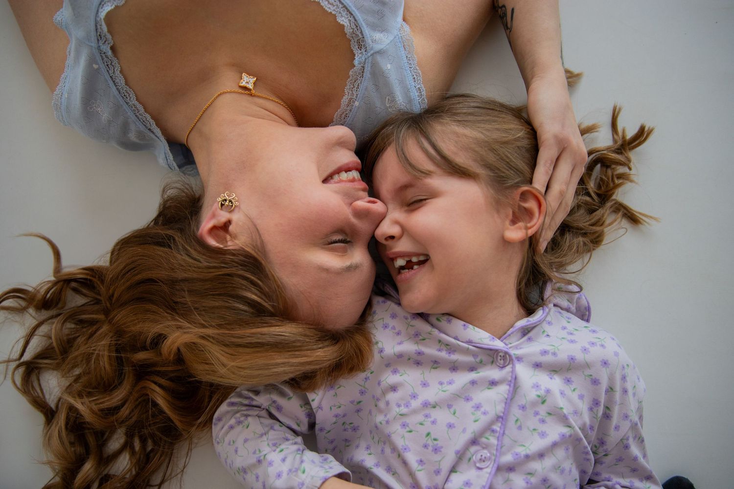 Joyful mother and young daughter laughing together while lying down face to face.