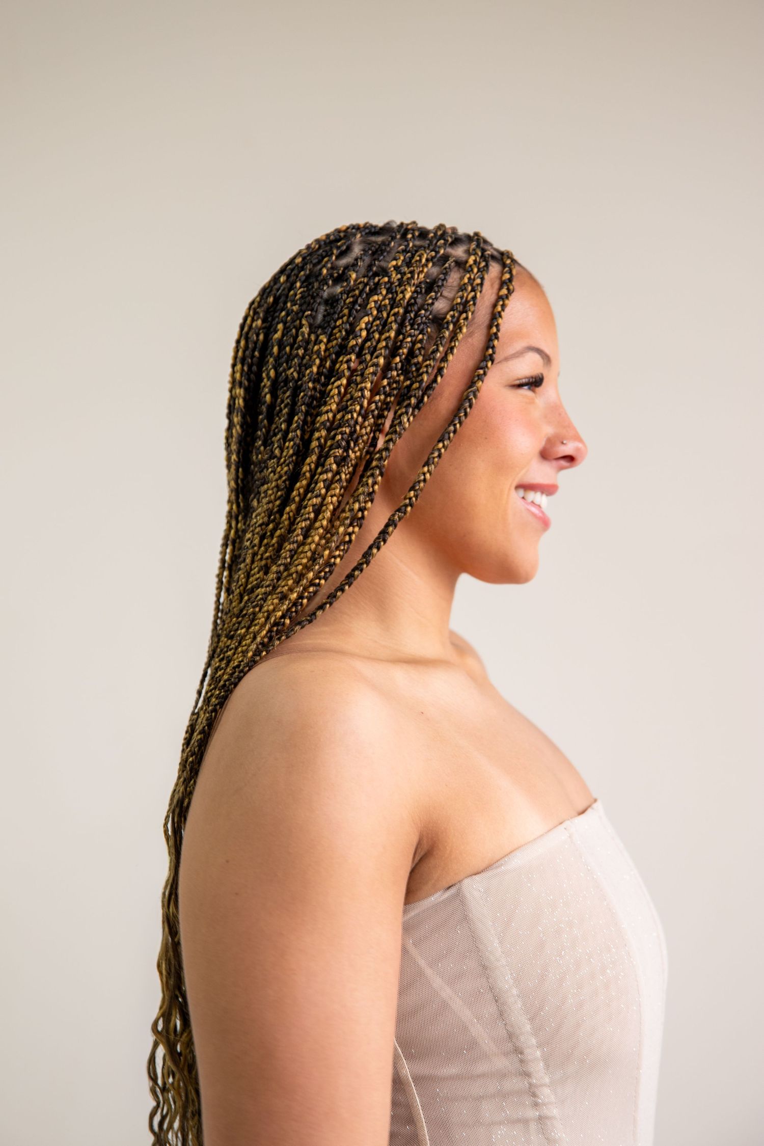Side profile of a young woman with long braided black and gold hair smiling against a gray background.