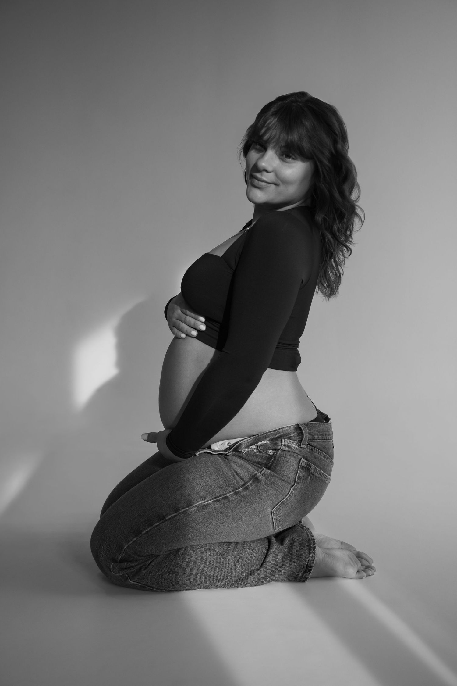 Black and white portrait of smiling pregnant woman kneeling and holding her baby bump.