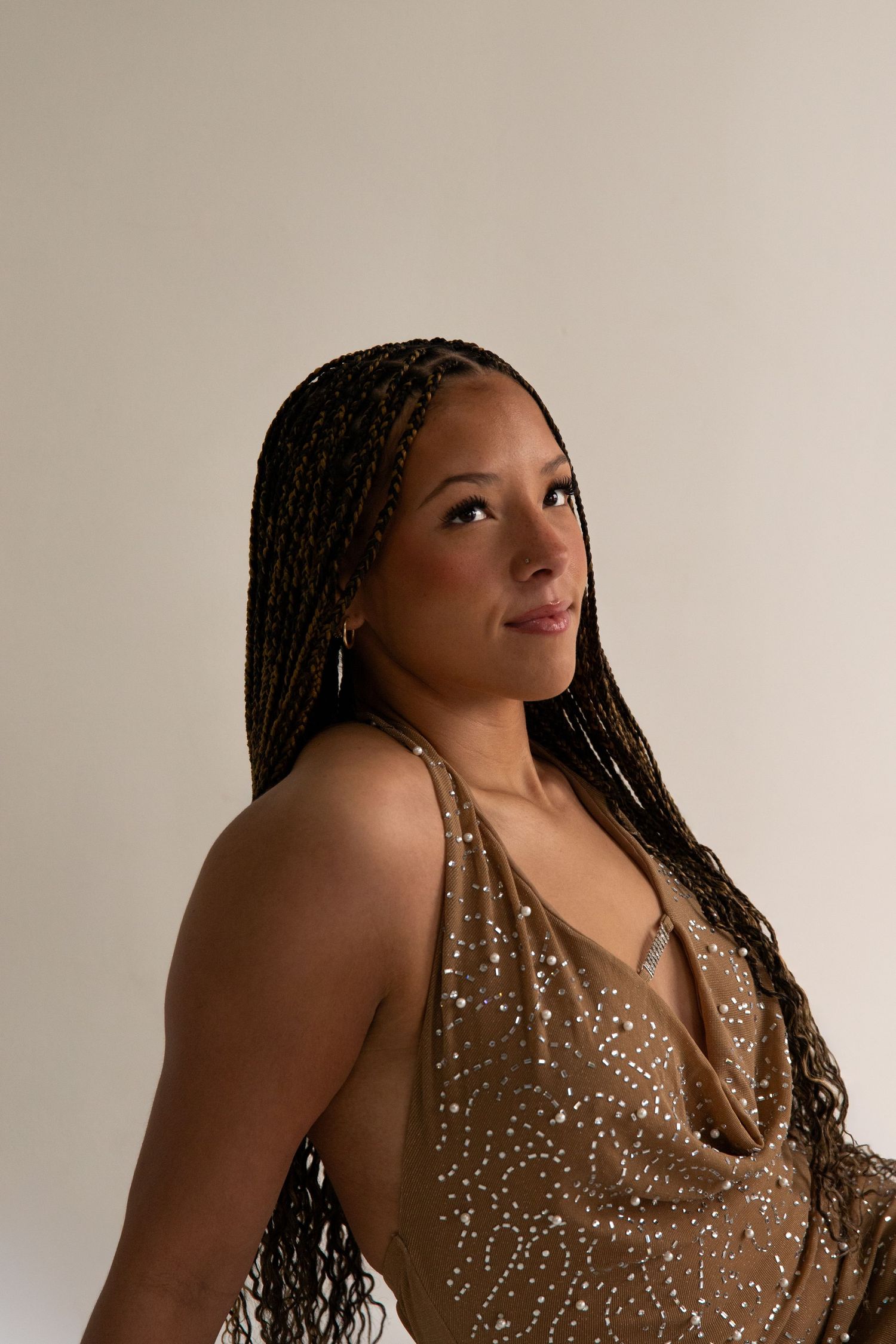 Woman with long box braids in a gold sparkly dress posing confidently in a studio setting.