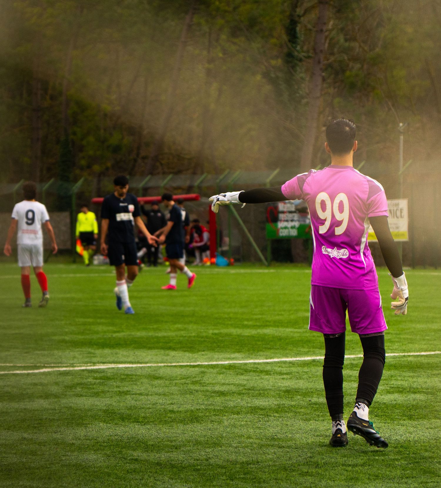 Soccer goalkeeper in purple jersey number 99 directing teammates during a match on a green field.