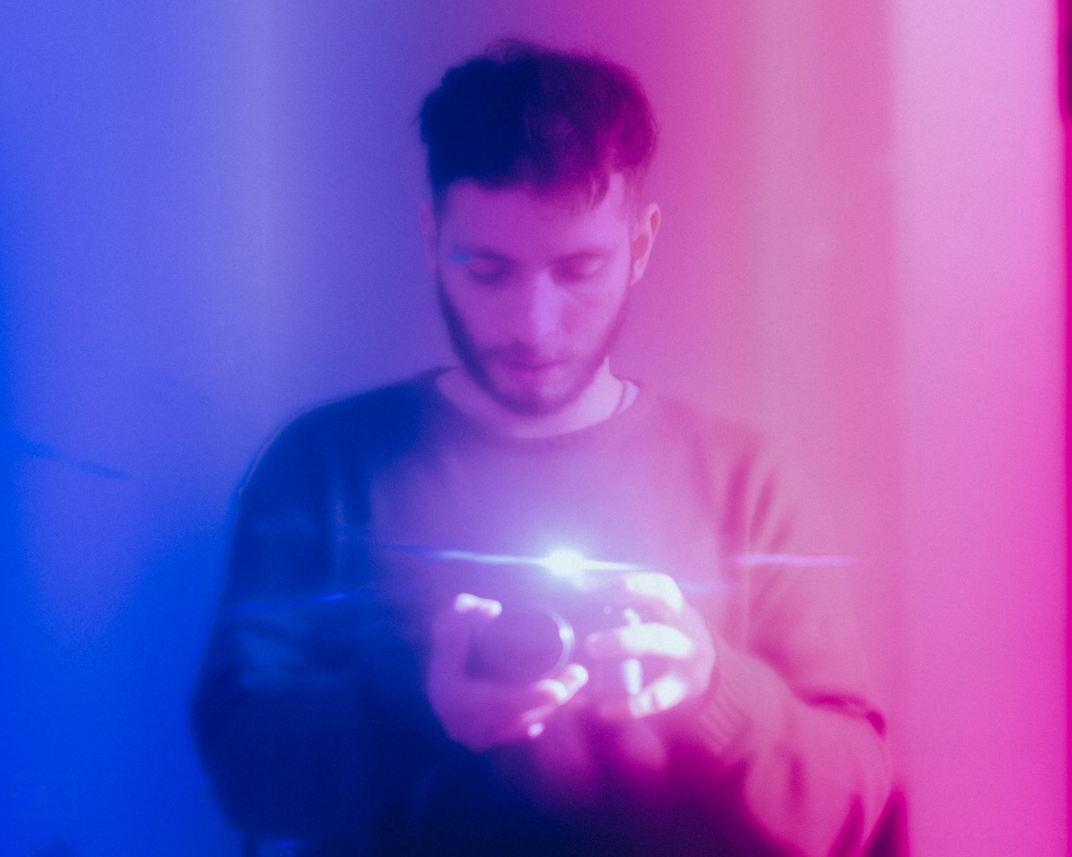 Person holding glowing sparklers creating a magical light trail effect against a purple and pink illuminated background.
