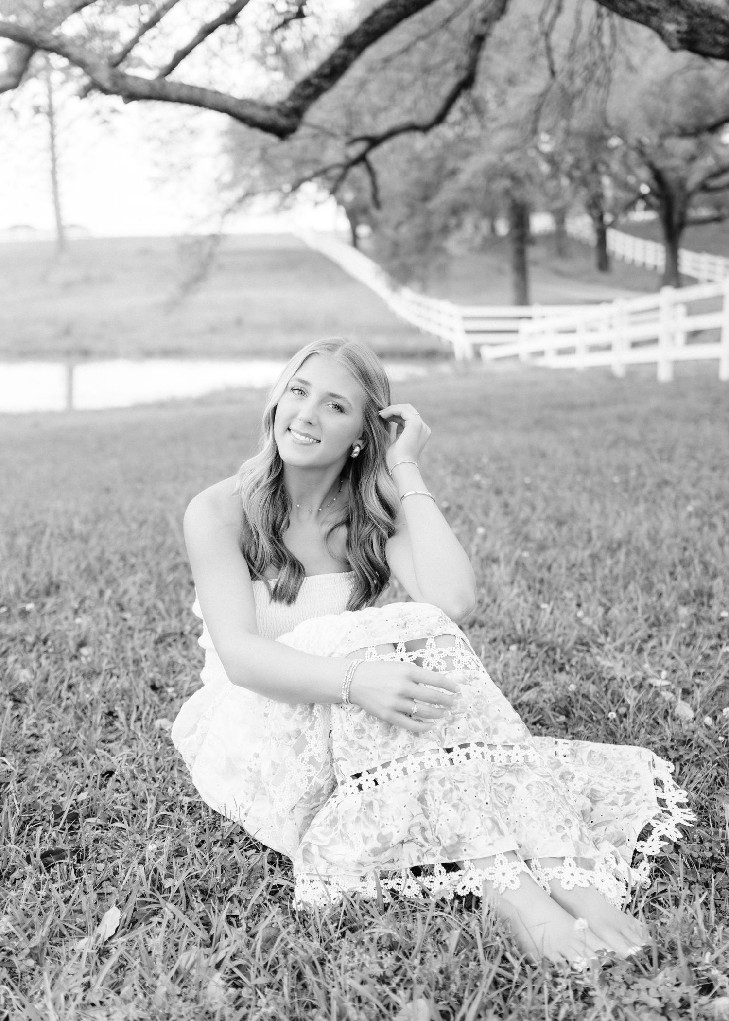 Black and white photo of smiling young woman sitting on grass in lace dress.