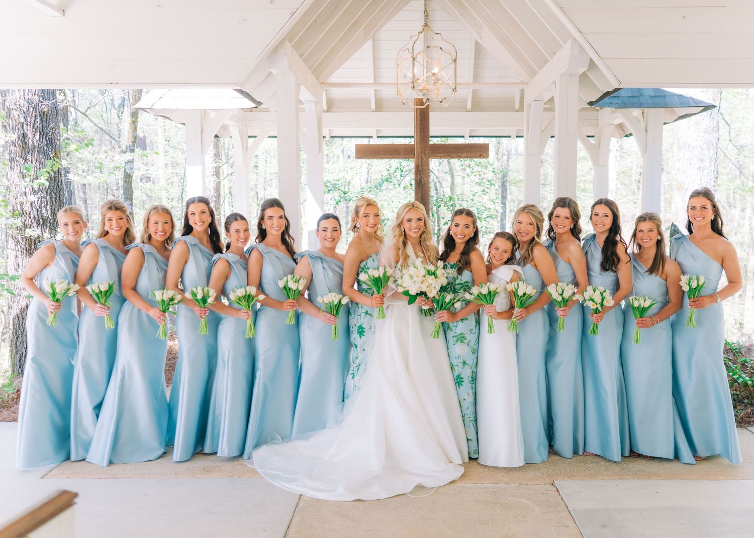 Bride in white gown stands with bridesmaids in light blue dresses holding bouquets inside a chapel.