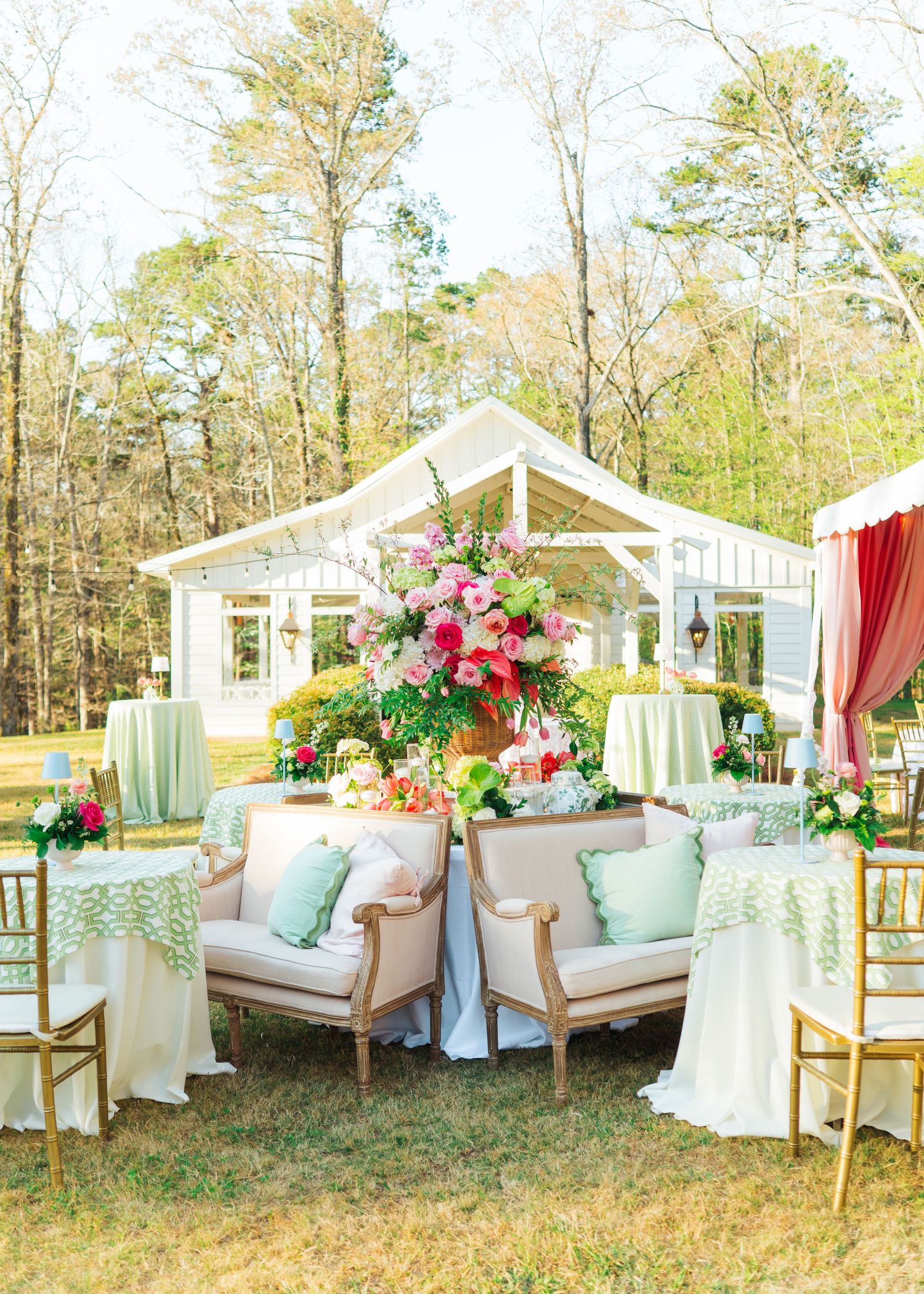 Elegant outdoor wedding reception with floral centerpiece, vintage sofas, mint green linens, and a white greenhouse backdrop.