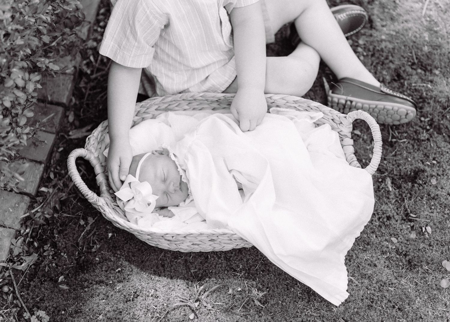 Newborn baby sleeping peacefully in wicker Moses basket outdoors in black and white photo.