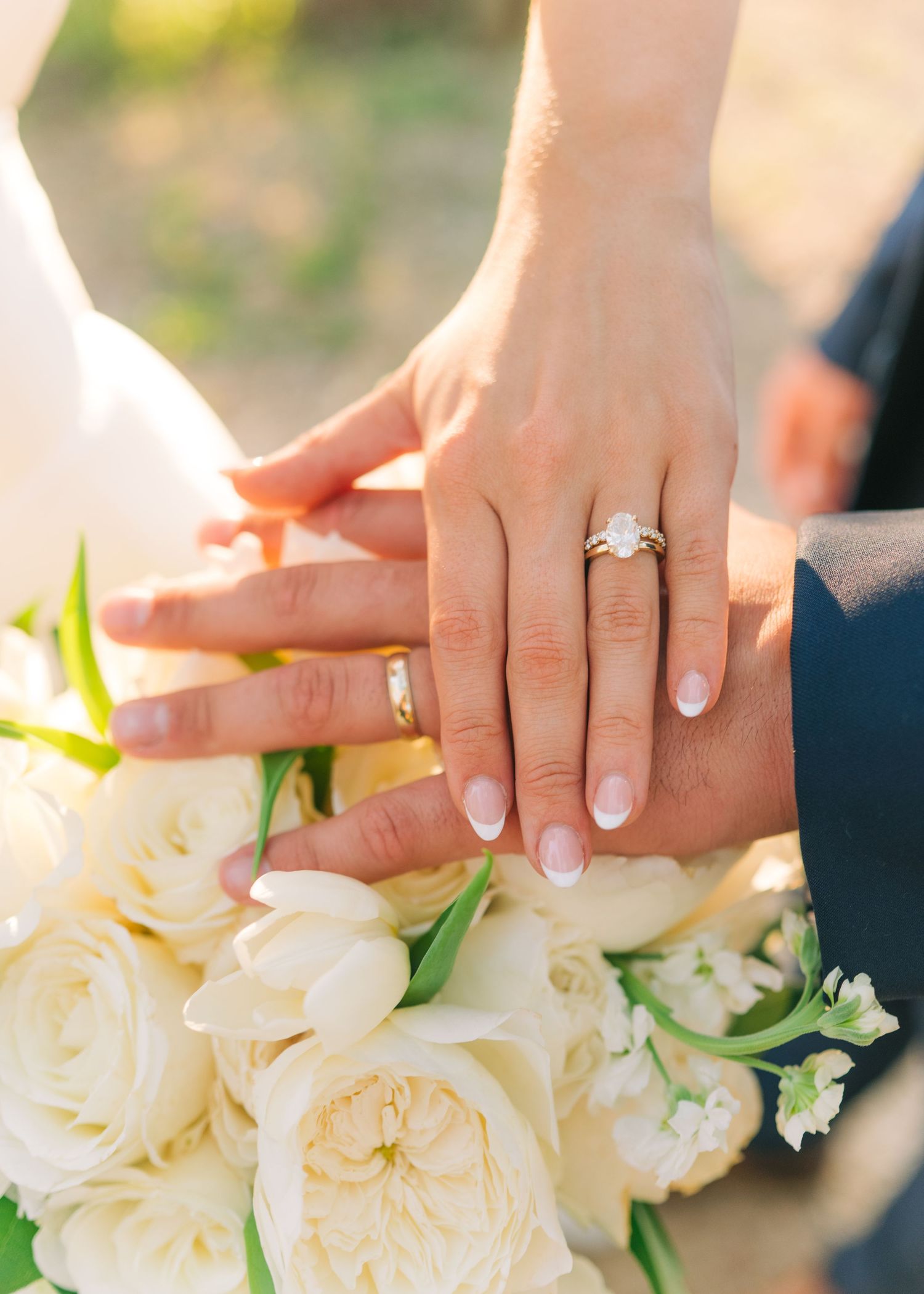 Bride and groom display wedding rings over white rose and tulip bouquet.