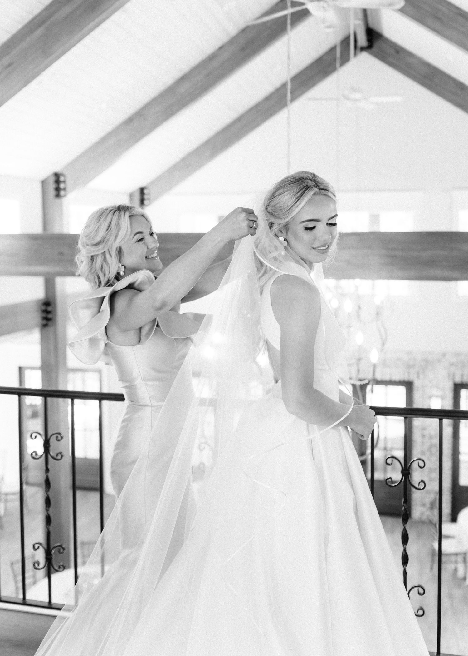 Bridesmaid attaching veil to bride in white gown in black and white wedding photo.