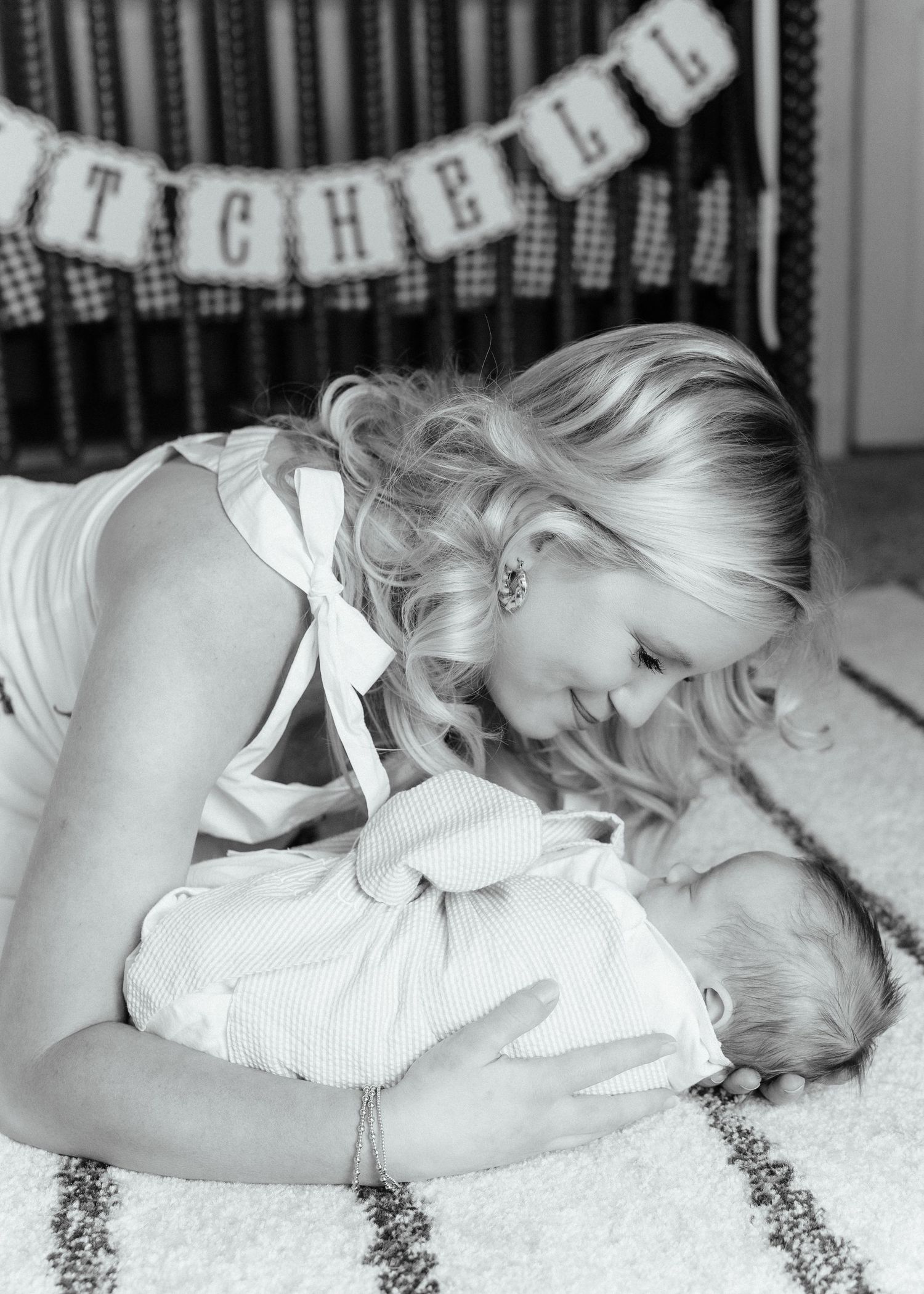 A blonde mother tenderly gazes at her newborn baby in a black and white photo.