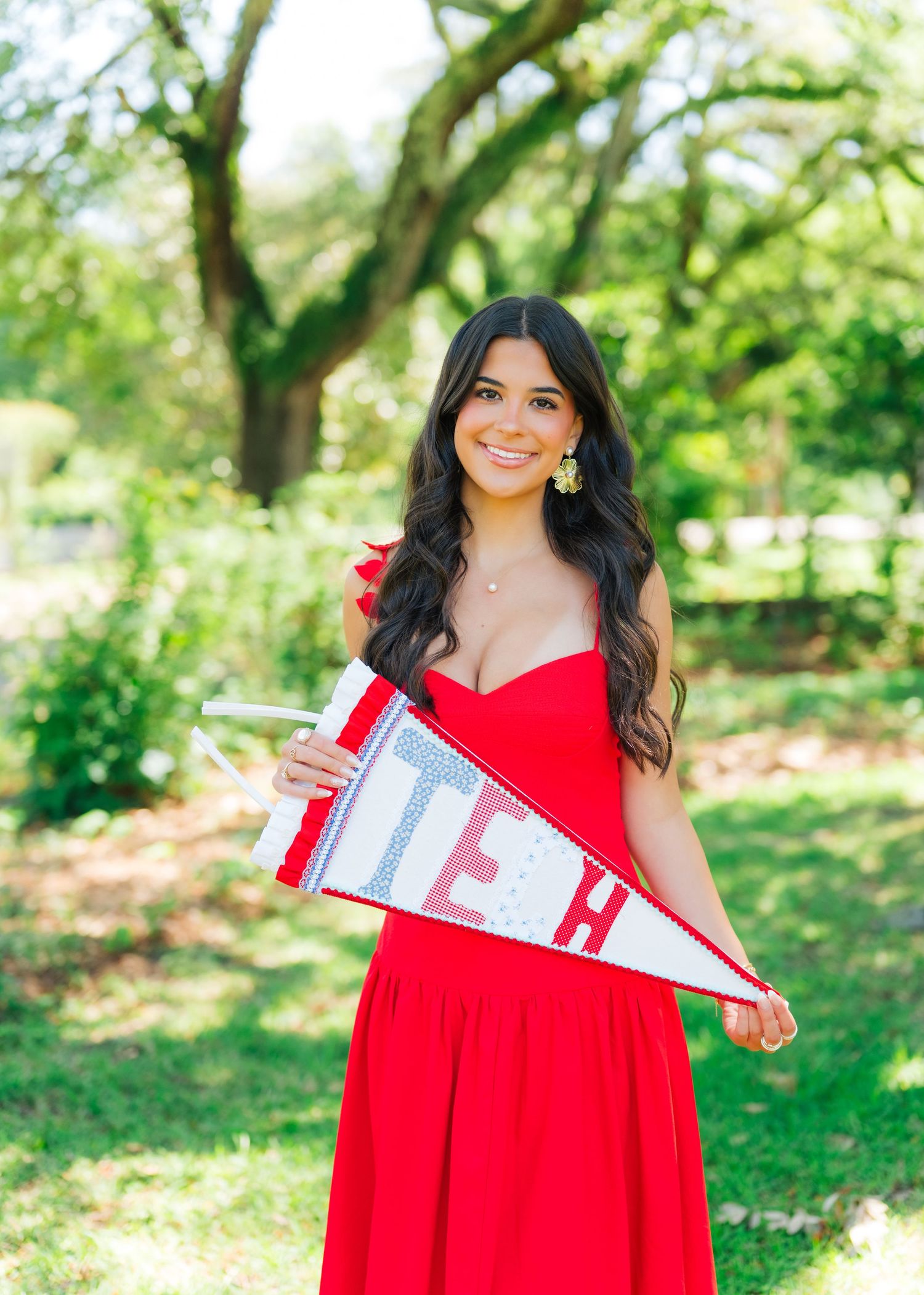 Smiling woman in red strapless gown holds TEX pennant flag outdoors.