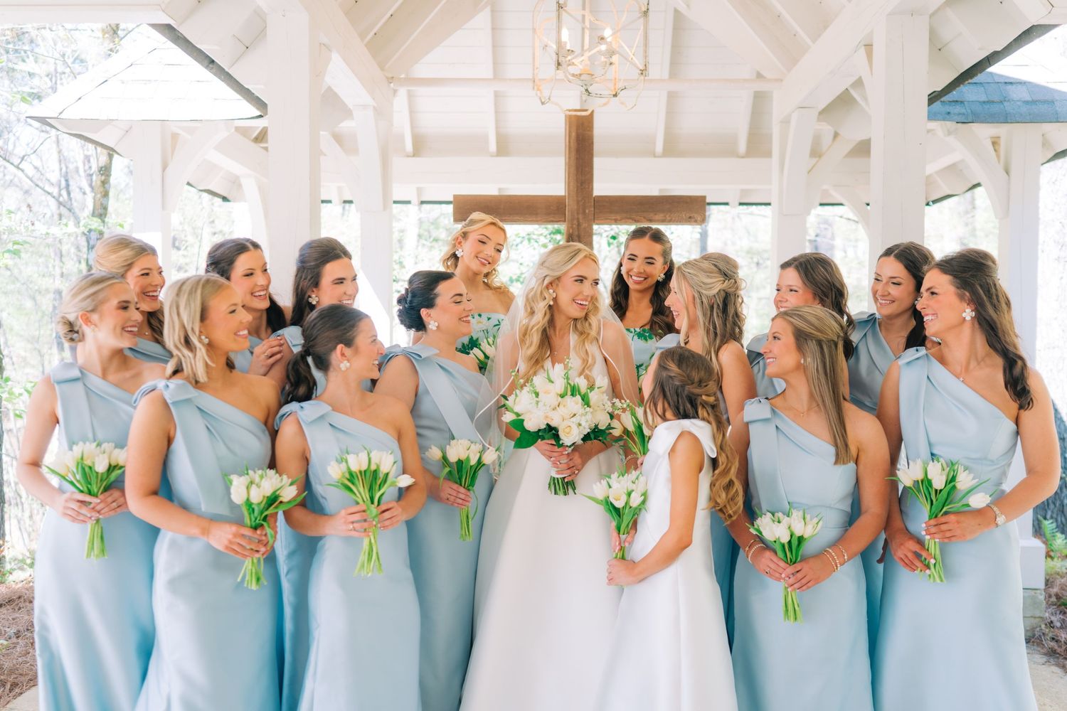 Bride in white gown surrounded by bridesmaids in light blue dresses holding white bouquets.