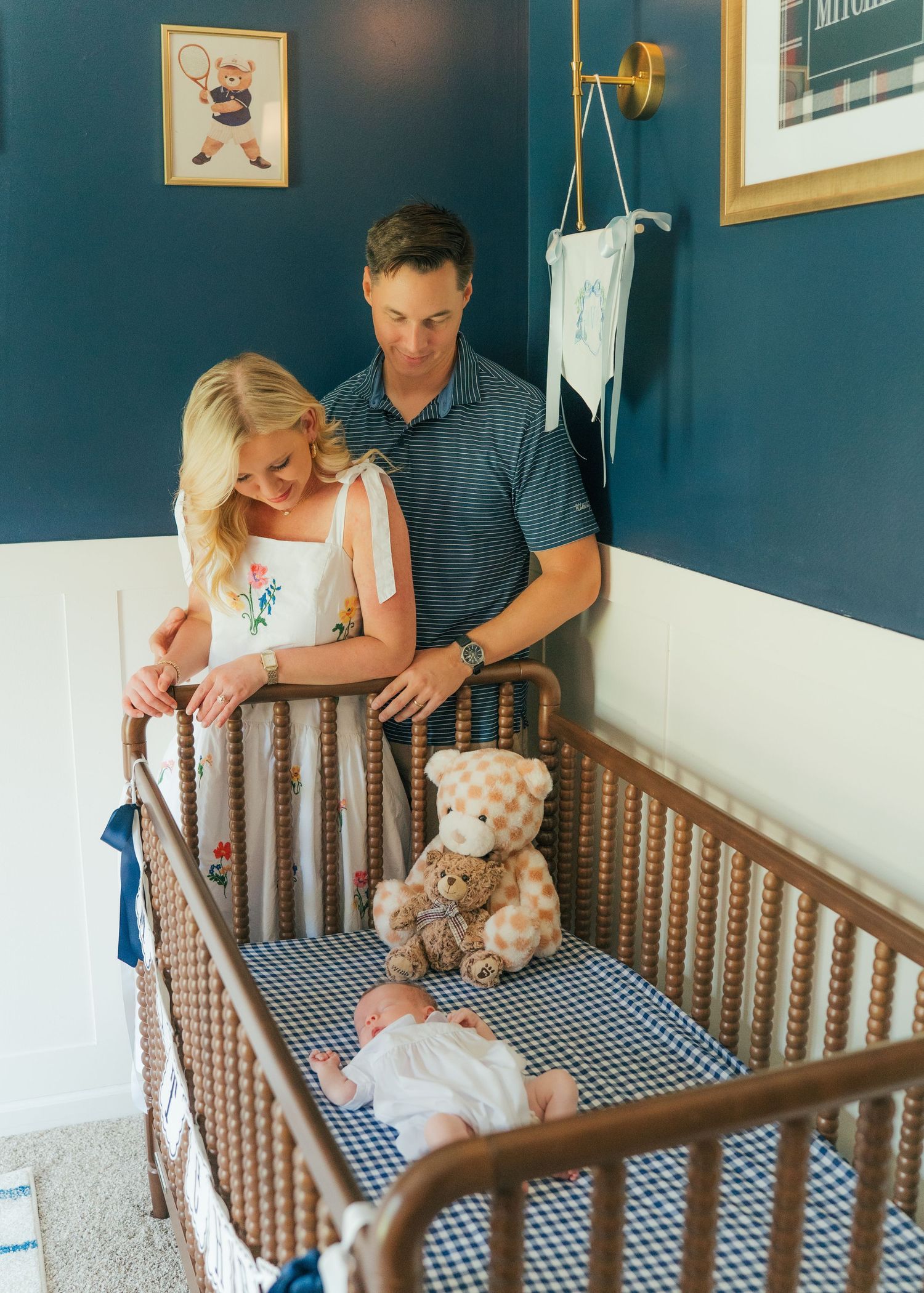 Parents lovingly gaze at their newborn in a navy blue nursery with a classic wooden crib.