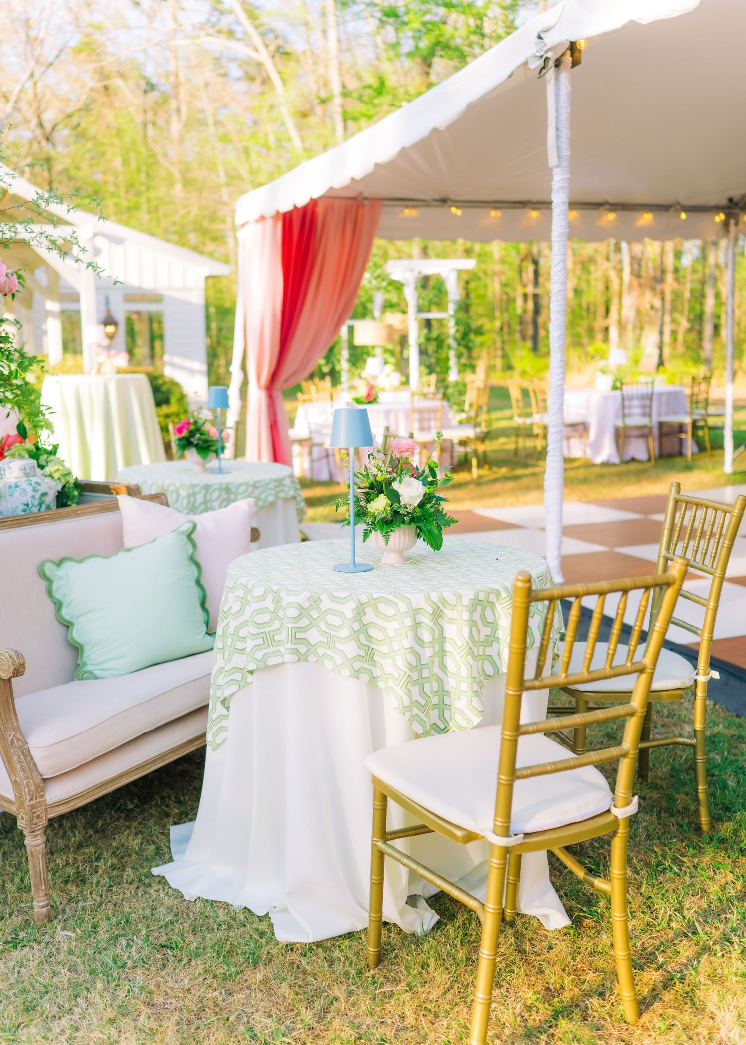 Colorful outdoor wedding reception with green patterned tablecloth, gold chairs, and floral centerpiece.