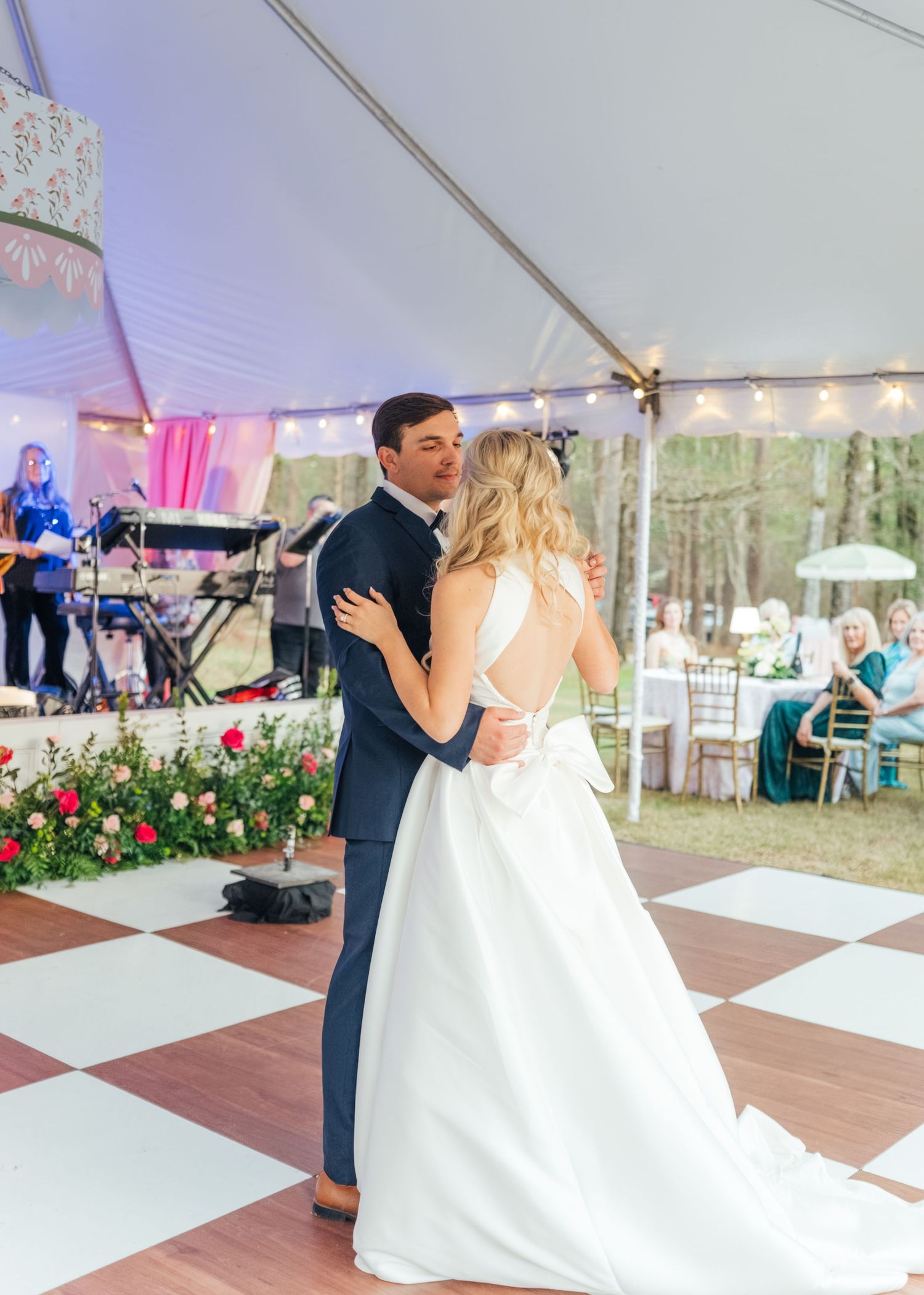 Bride and groom share their first dance under a tent with string lights at an outdoor wedding reception.