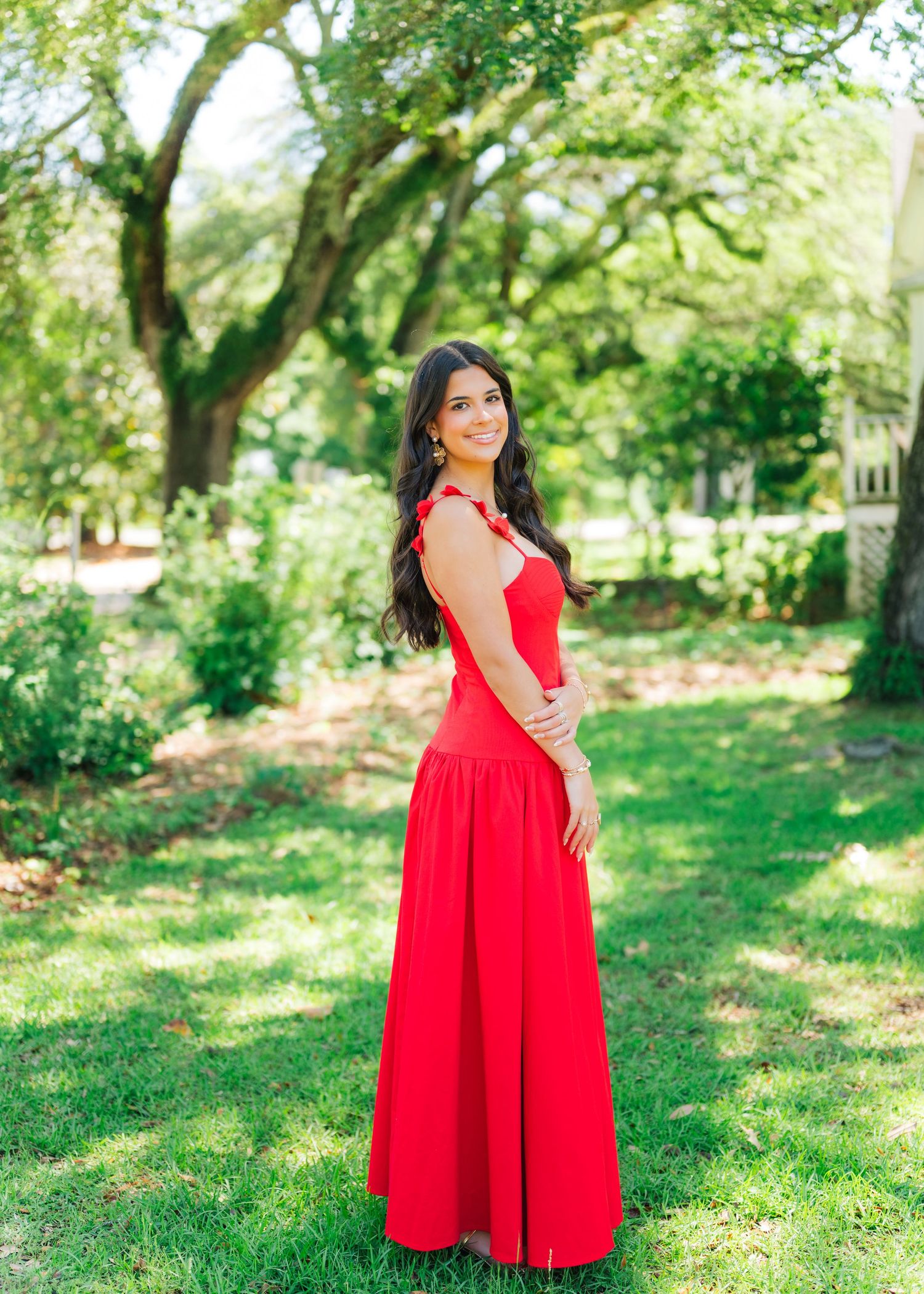 Brunette woman in red sleeveless maxi dress smiles in sunny garden.