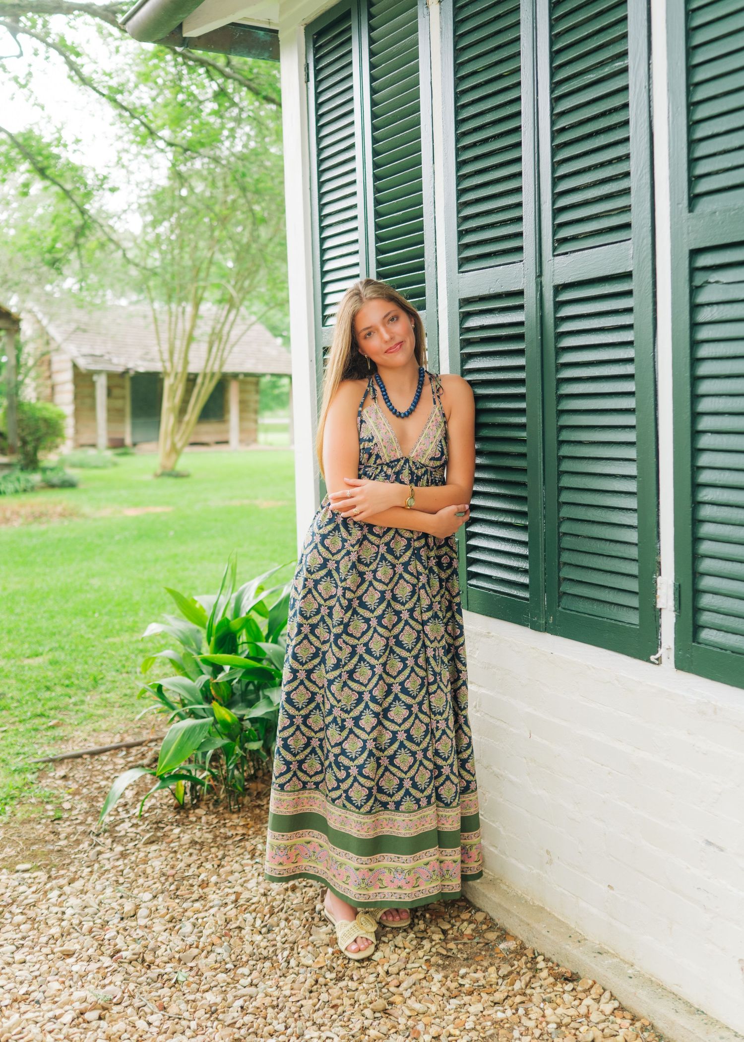 Young woman in bohemian maxi dress posing by green shutters on a white porch.