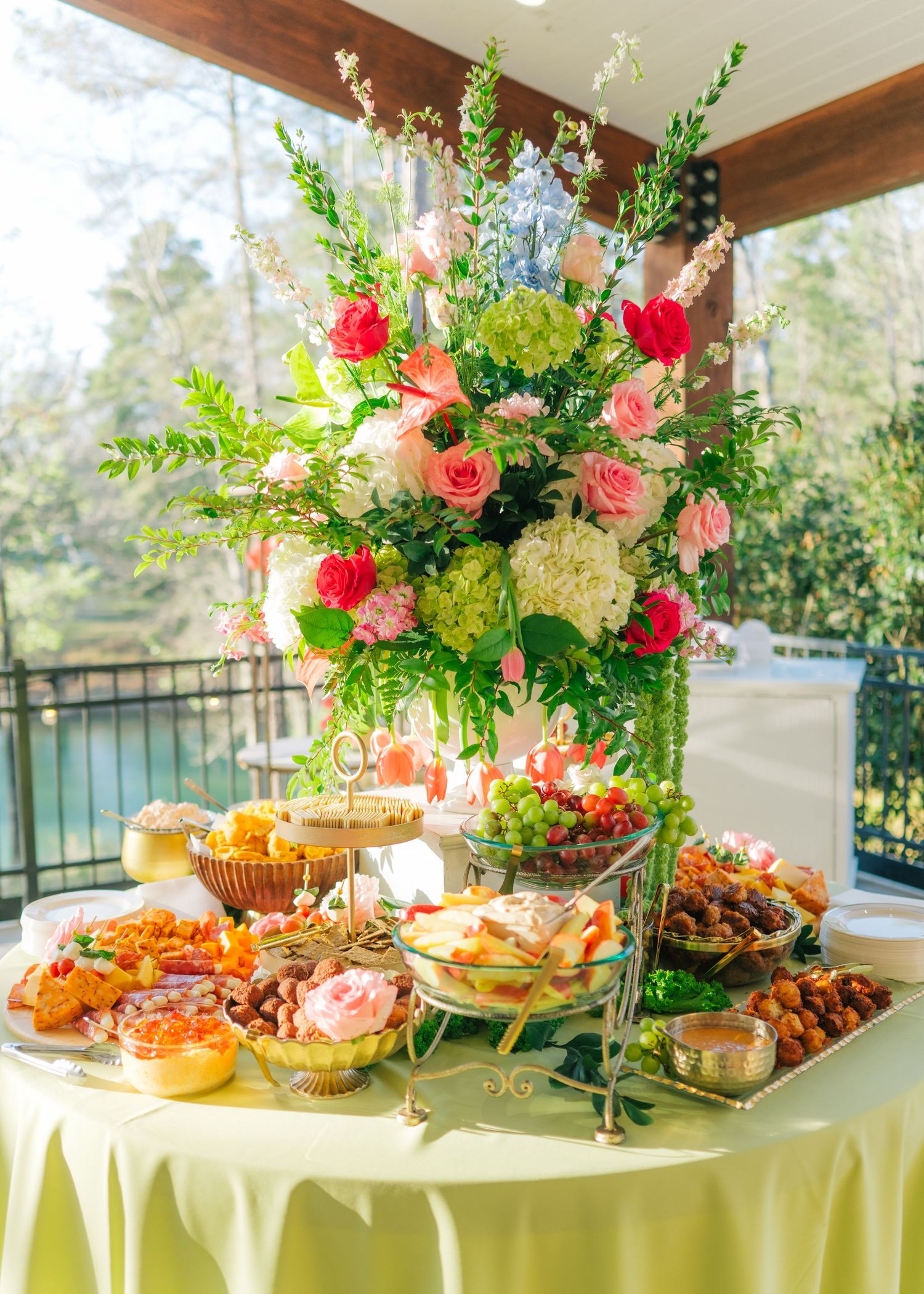 Elegant wedding food table with tall pink and white floral arrangement and assorted appetizers.