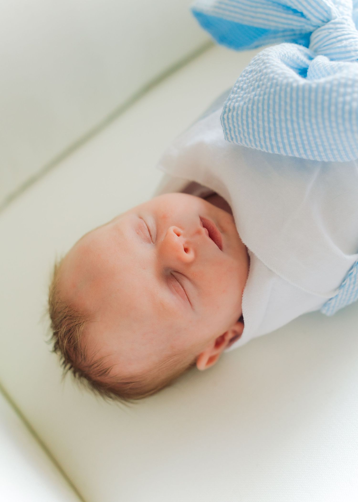 Peaceful newborn baby sleeping wrapped in white and blue blanket on a soft white surface.