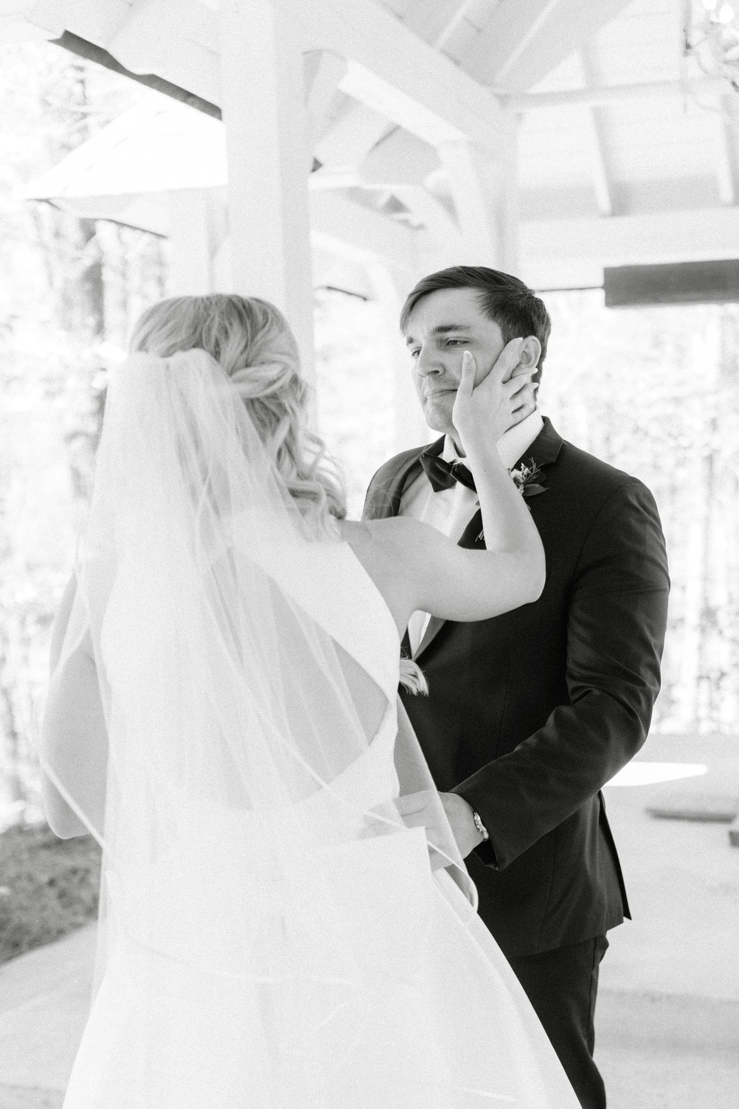 Black and white photo of bride touching grooms face during emotional first look at outdoor wedding venue.