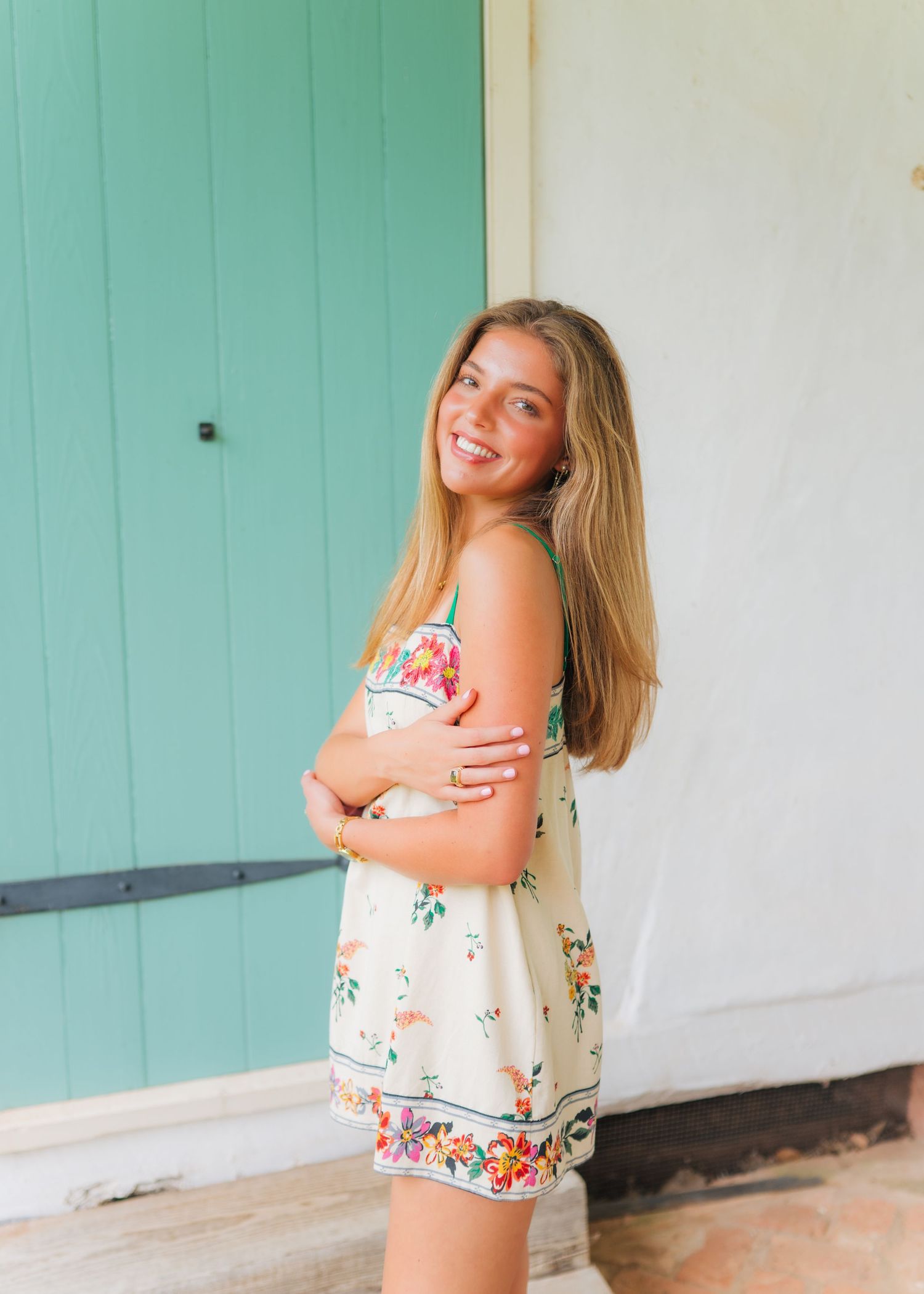 Smiling young woman in floral romper posing by teal door outdoors.