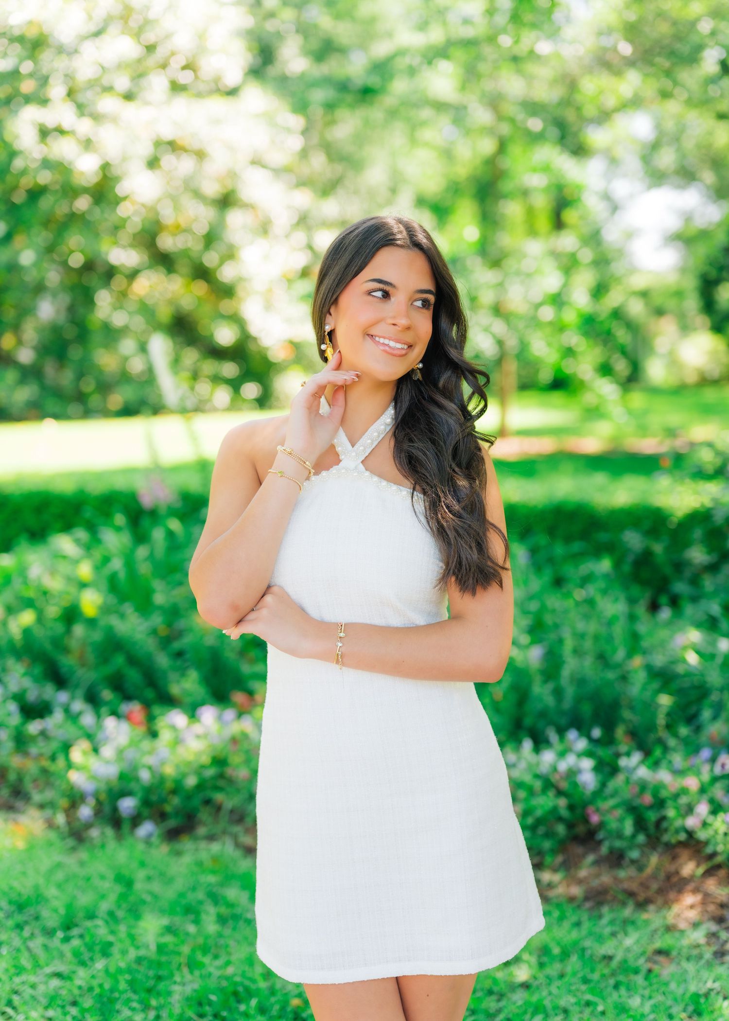 Young woman in white halter mini dress smiling outdoors in lush green garden setting.