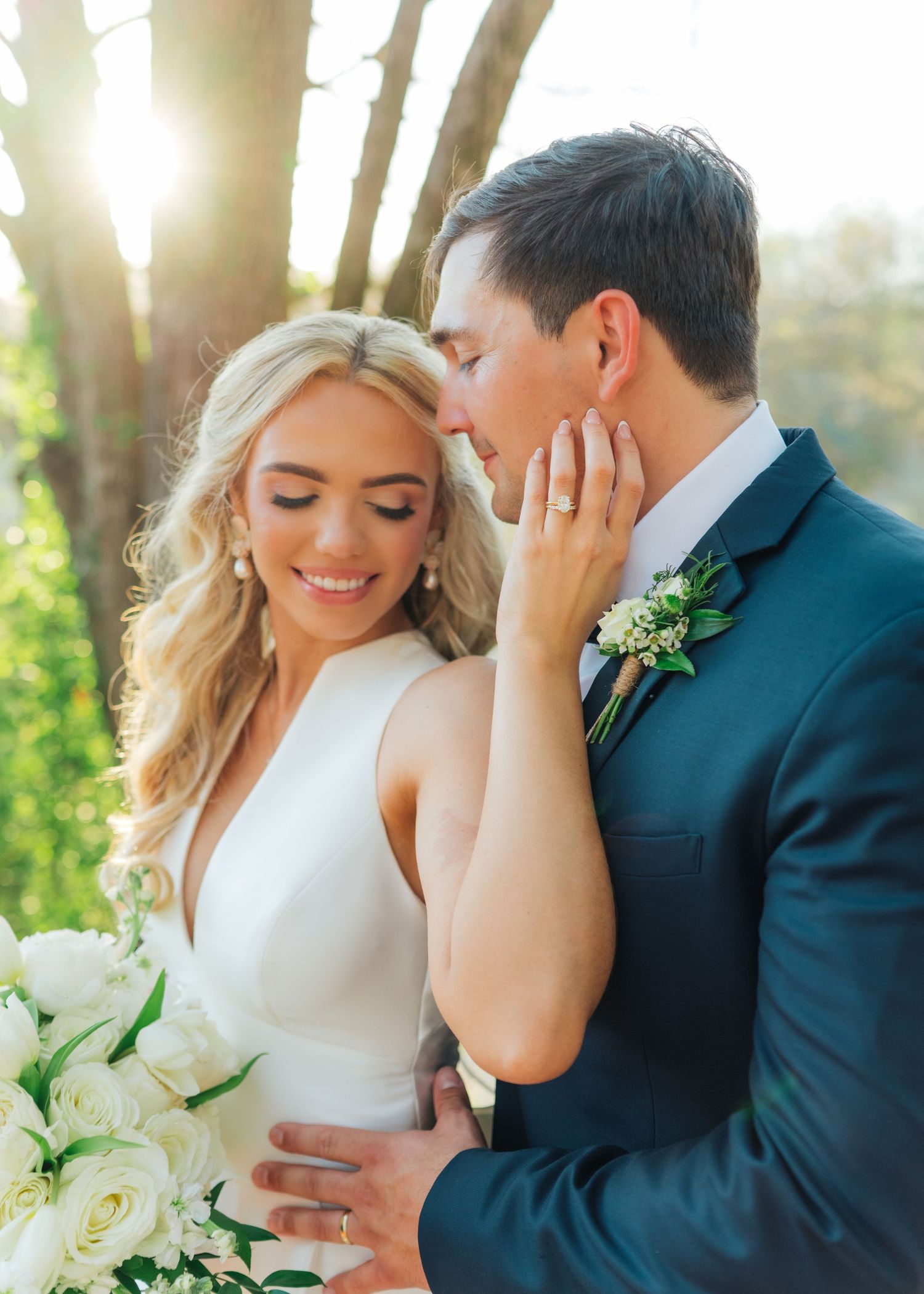 Bride and groom sharing romantic moment in golden sunlight, bride holding white bouquet.