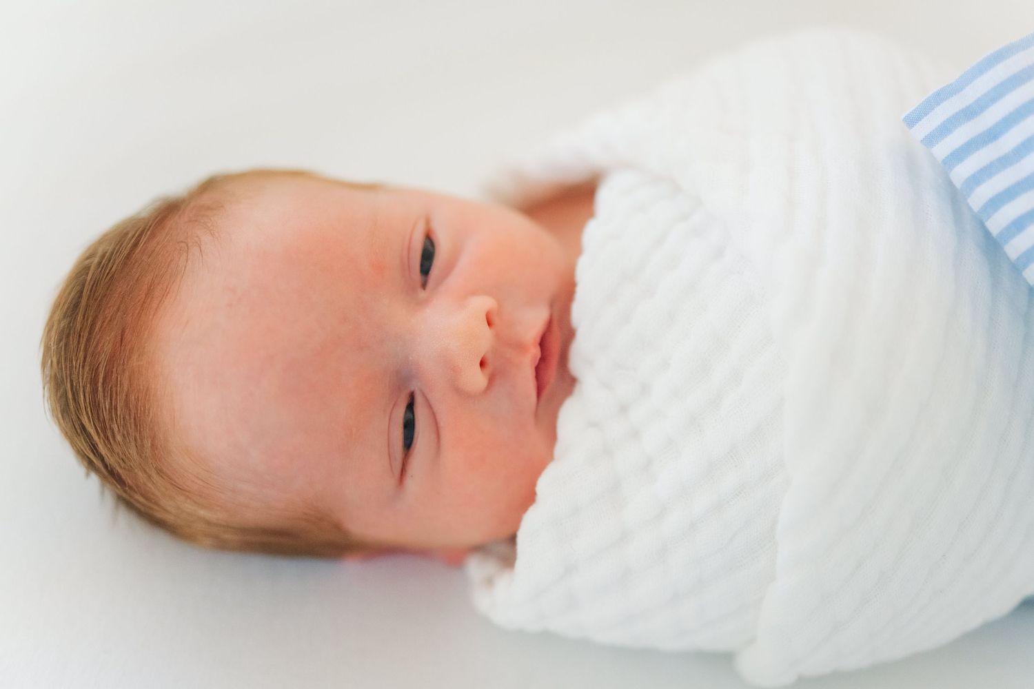 Close-up portrait of a peaceful swaddled newborn baby lying on a white surface.