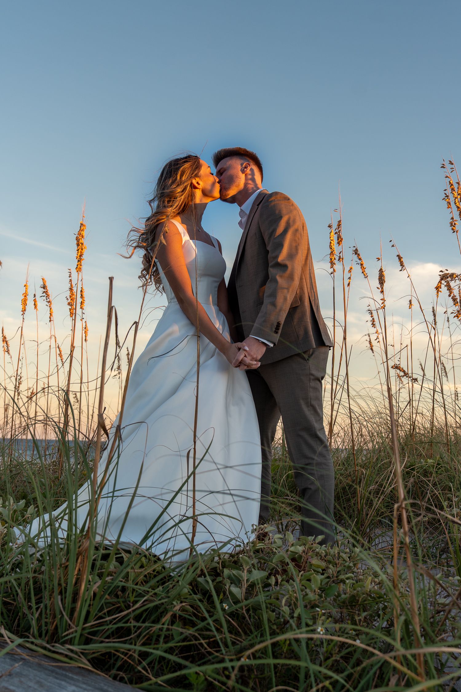 Bride and groom embracing in tall grass during a sunset wedding portrait session.