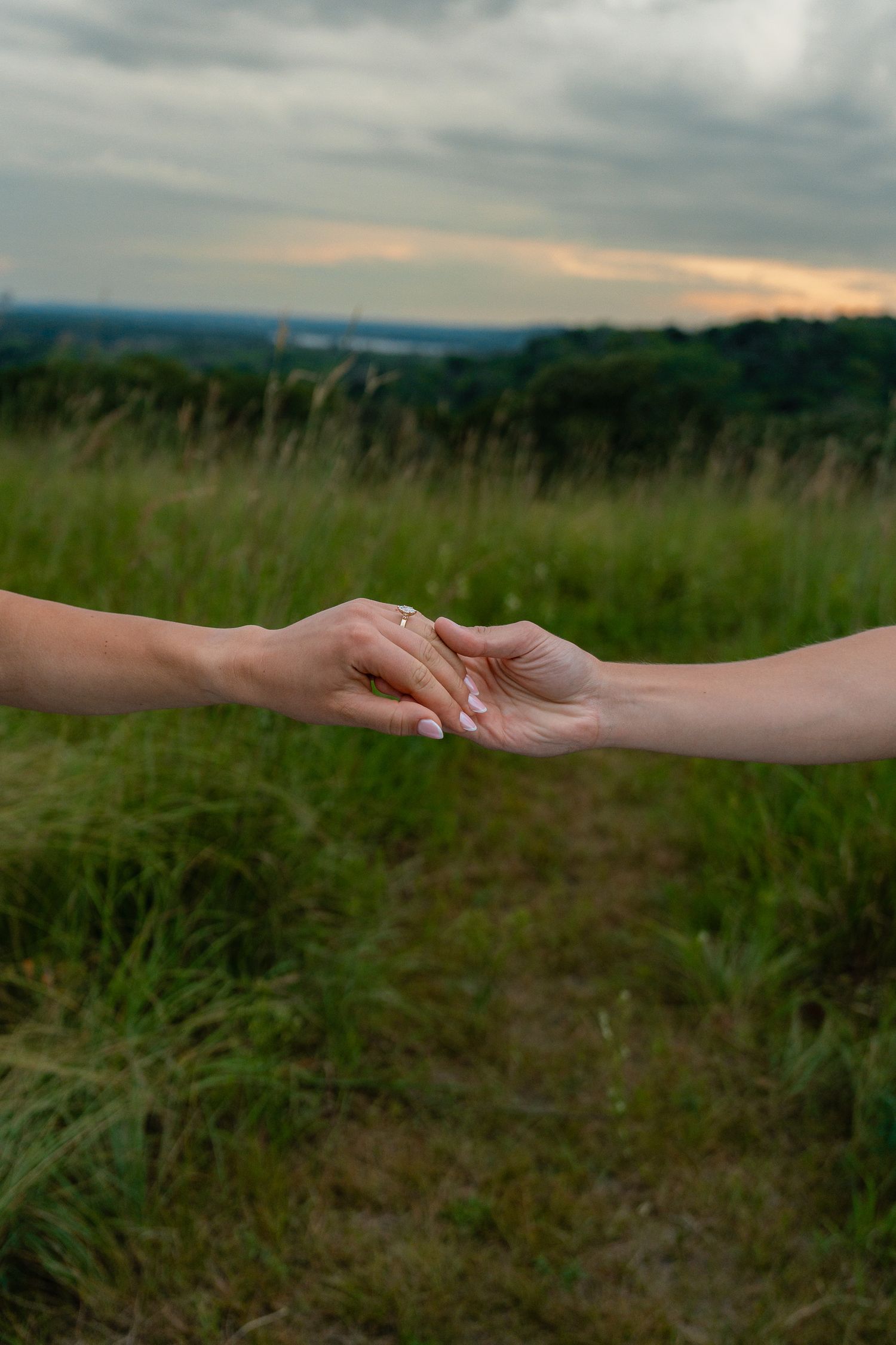 Close-up of a couple holding hands during an outdoor engagement session.