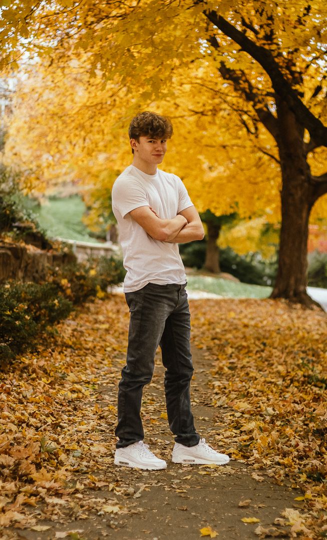 Person wearing a white t-shirt and dark pants stands amid vibrant yellow autumn foliage on the ground.
